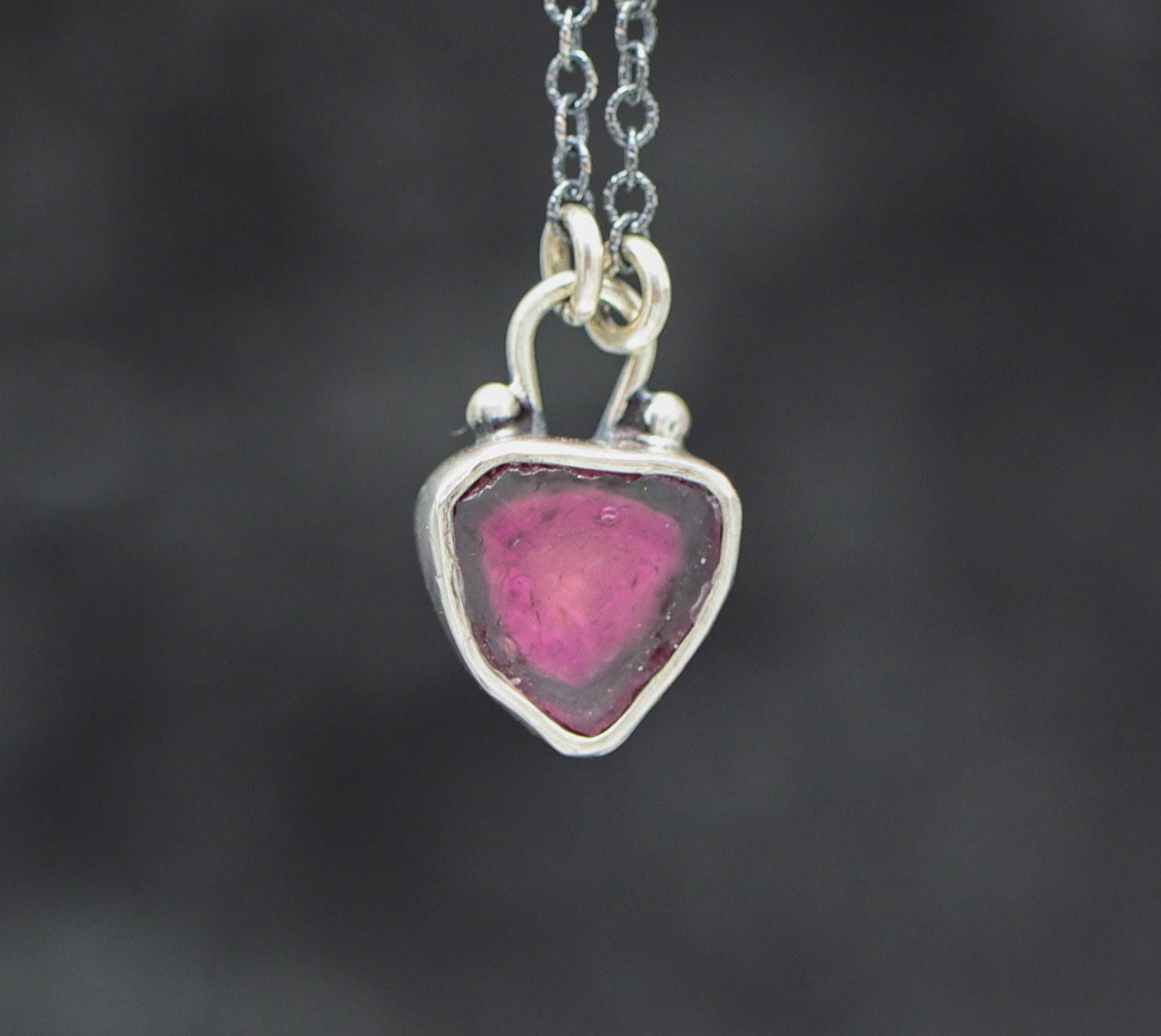 Silver necklace with a heart-shaped pink pendant on a dark background