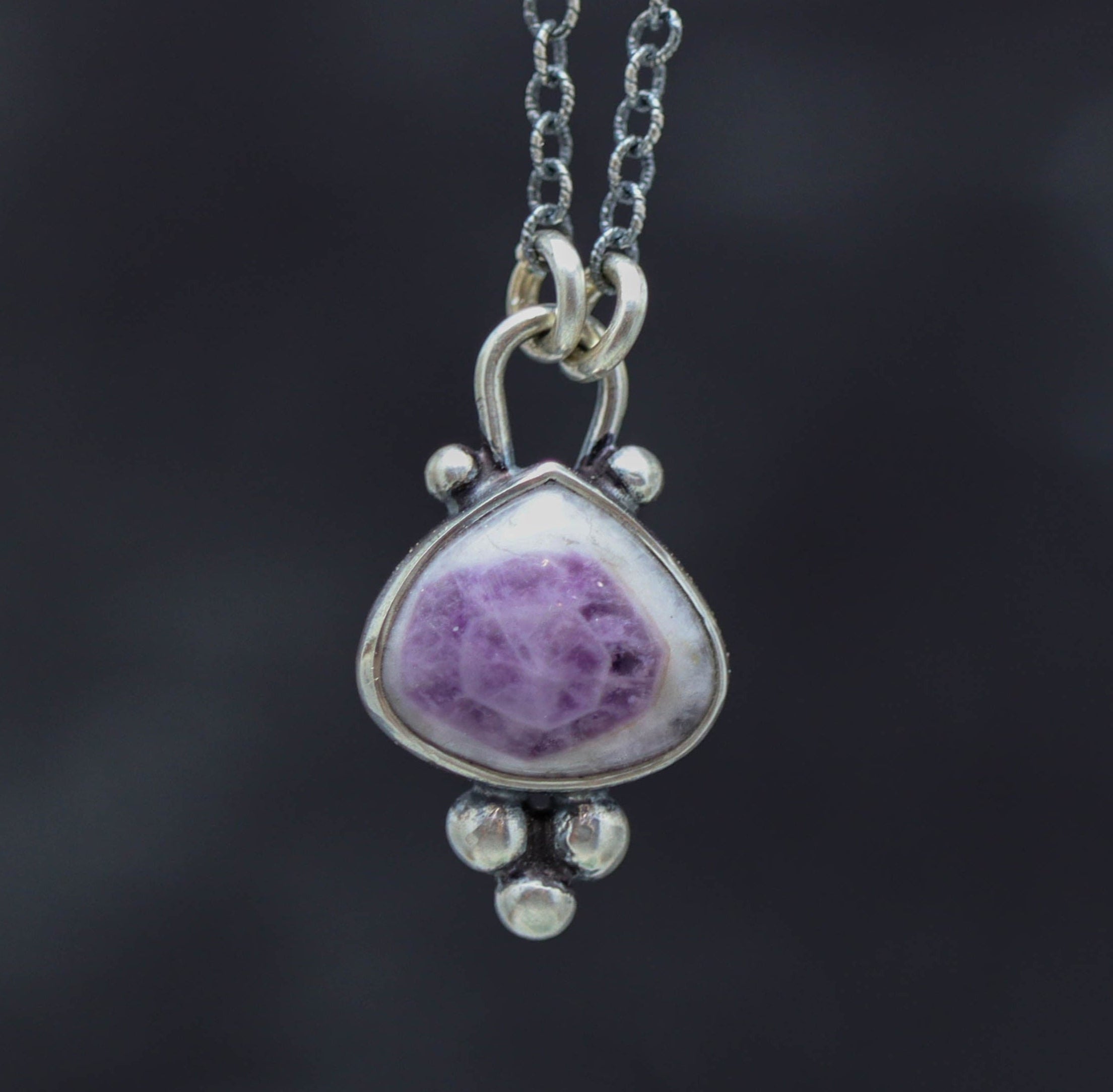 Silver pendant with a purple gemstone on a dark background