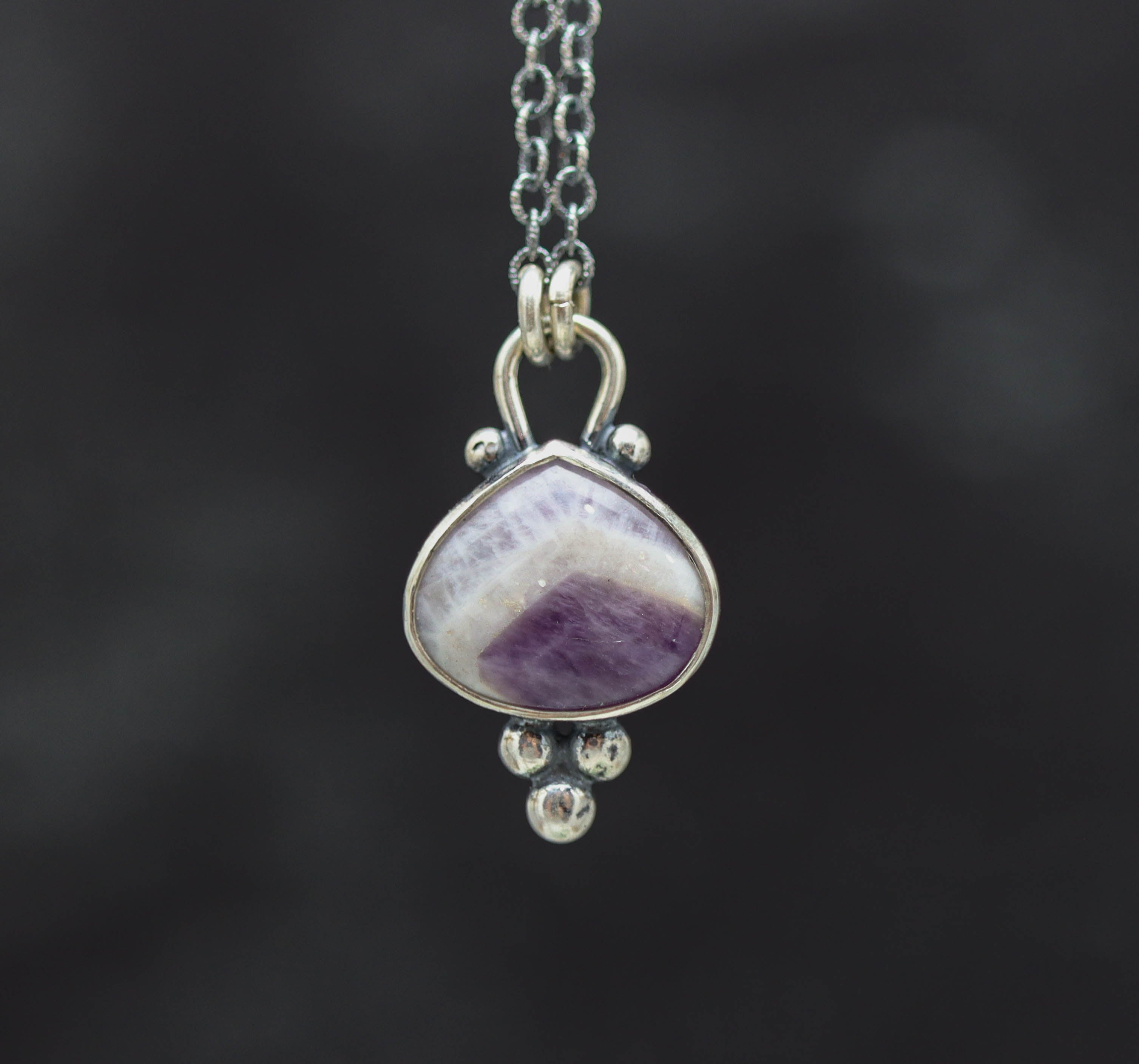 Silver pendant with a purple stone on a dark background
