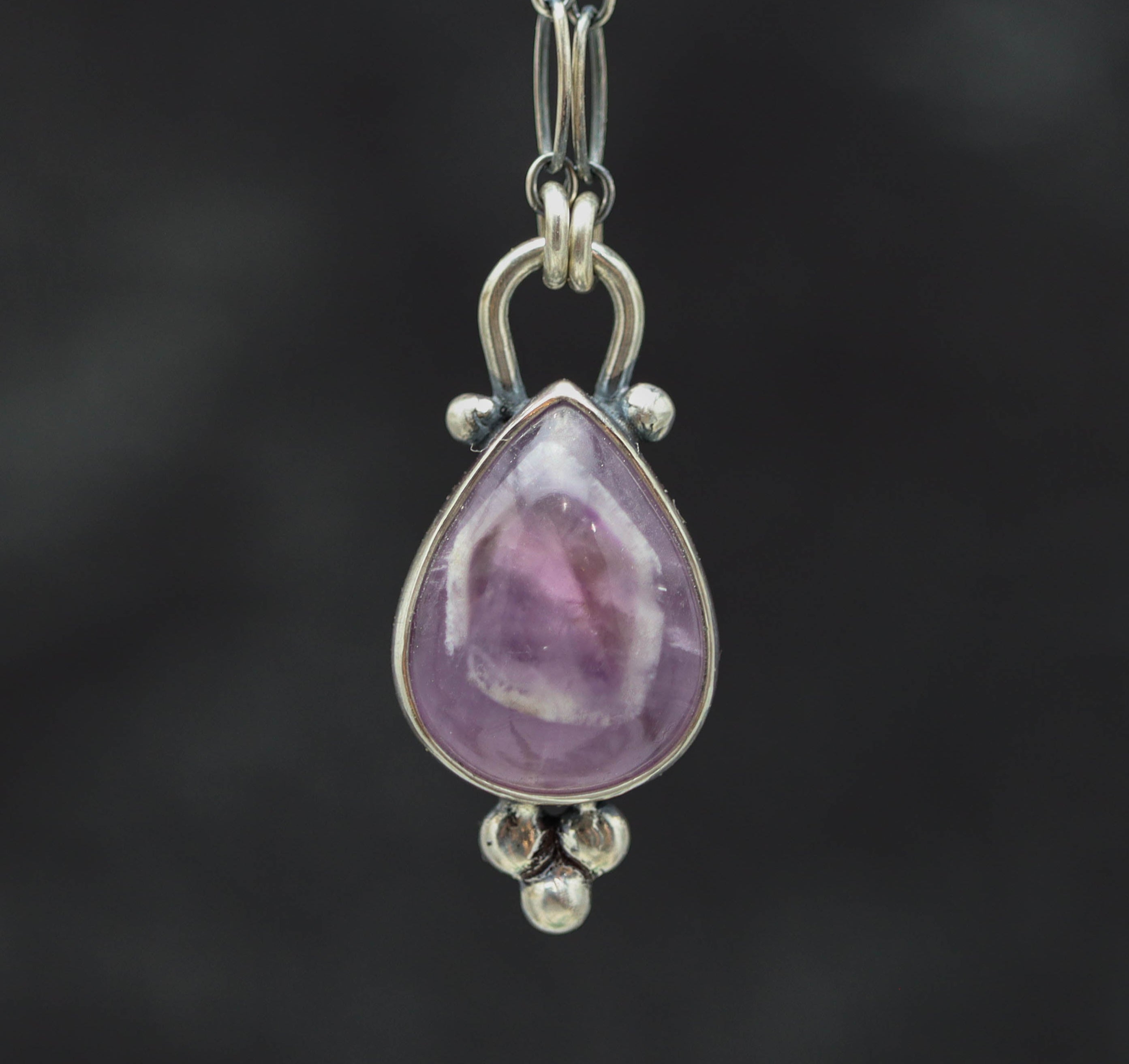 Teardrop-shaped purple gemstone pendant on a chain against a dark background