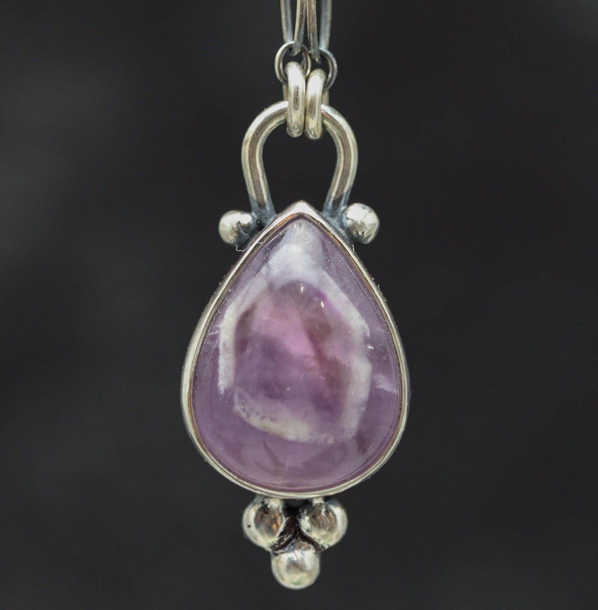 Teardrop-shaped purple gemstone pendant on a chain against a dark background