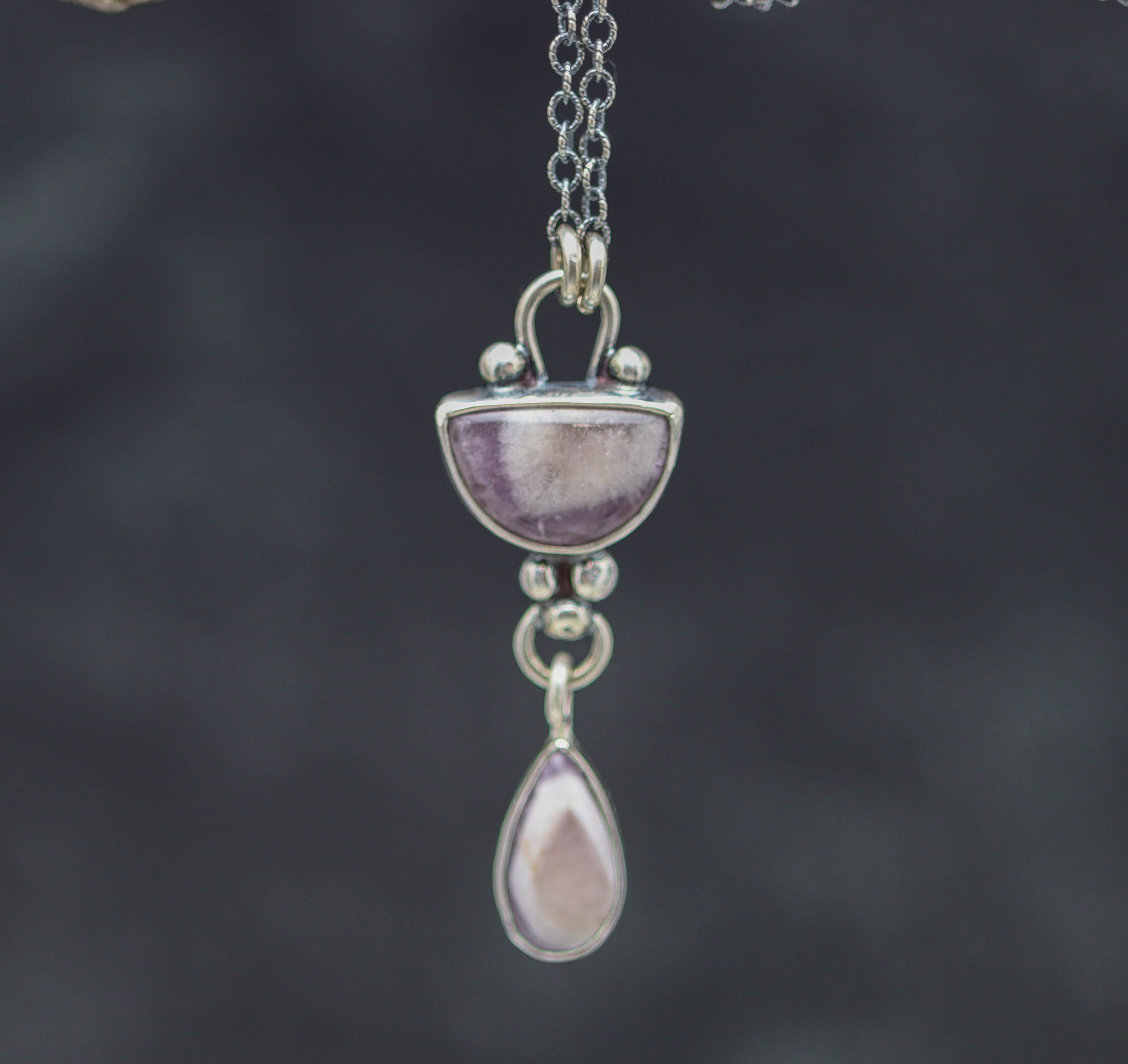Silver necklace with a pendant featuring purple stones on a dark background