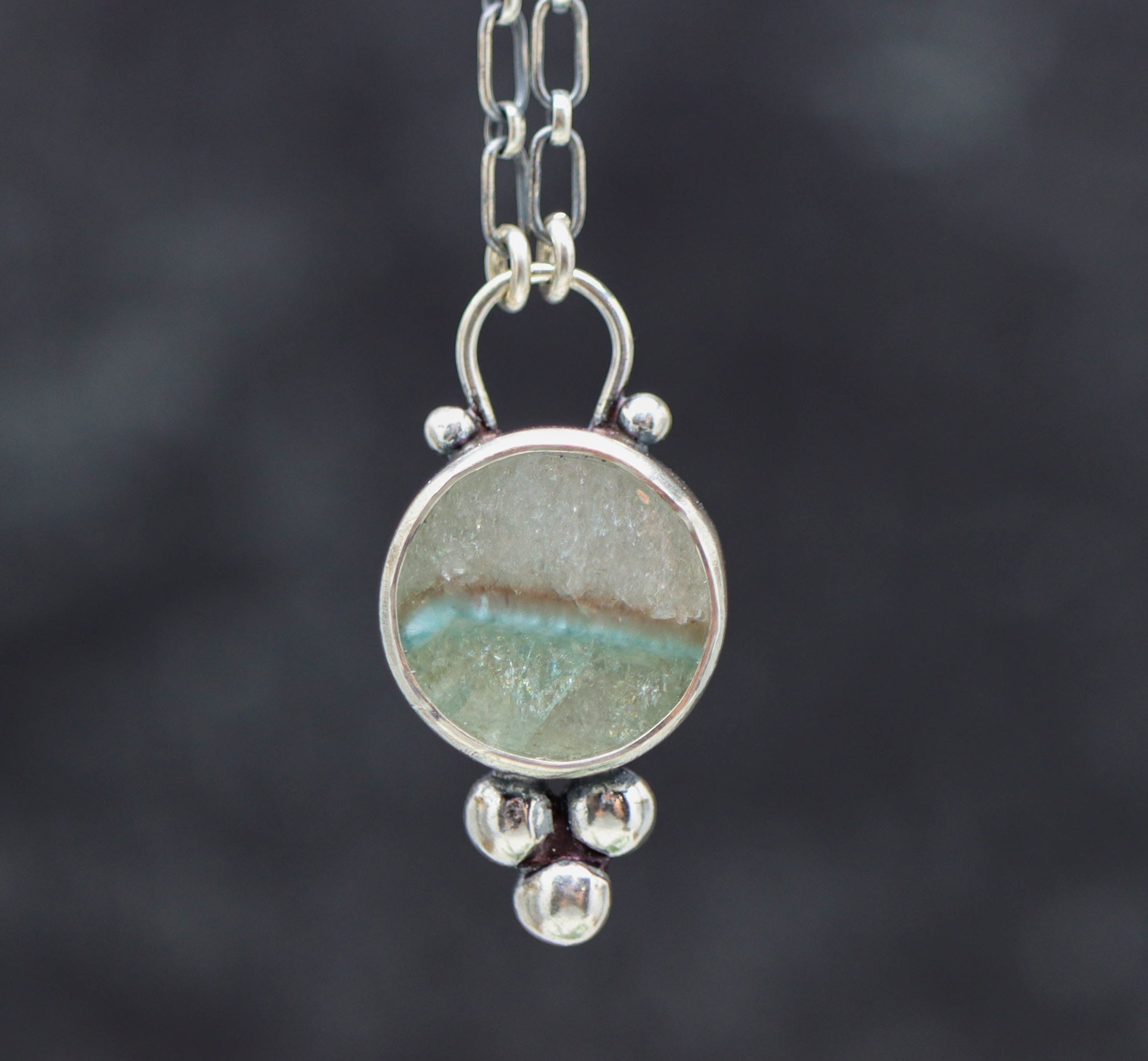 Silver necklace with a circular pendant featuring a natural stone on a dark background