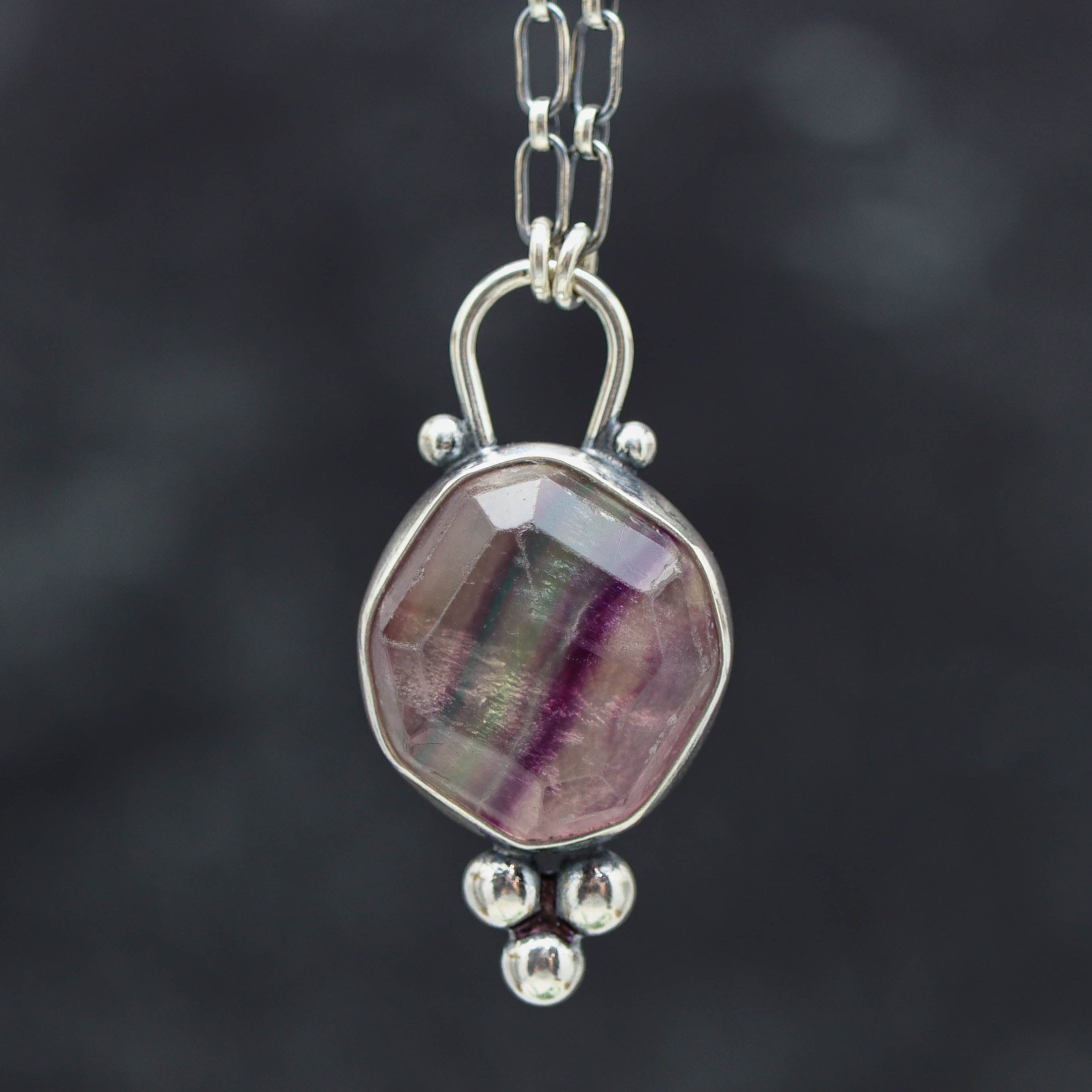 Silver pendant with a multicolored stone on a dark background