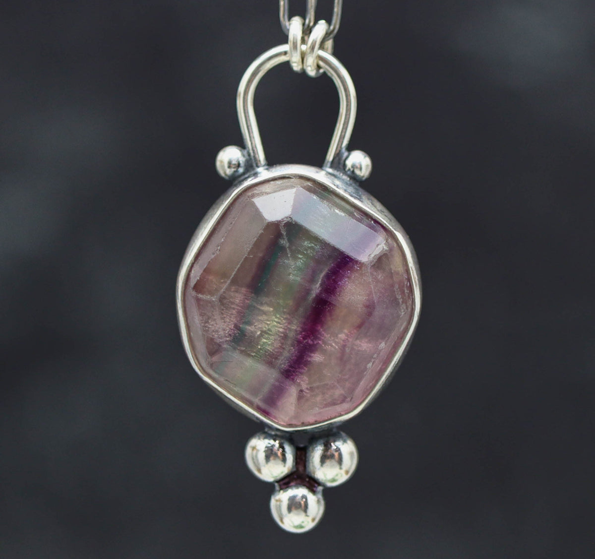 Silver pendant with a multicolored stone on a dark background