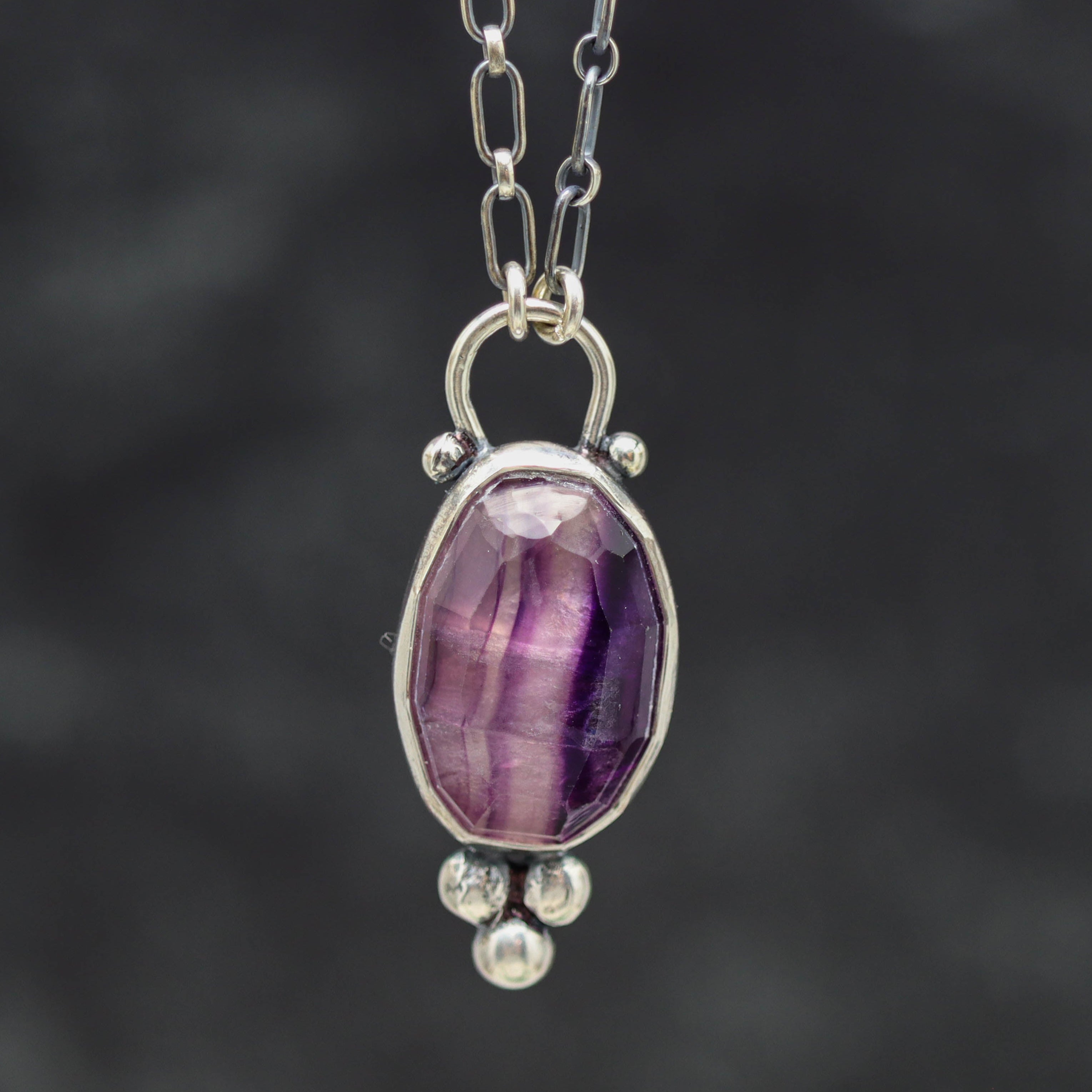 Silver pendant with a purple gemstone on a dark background
