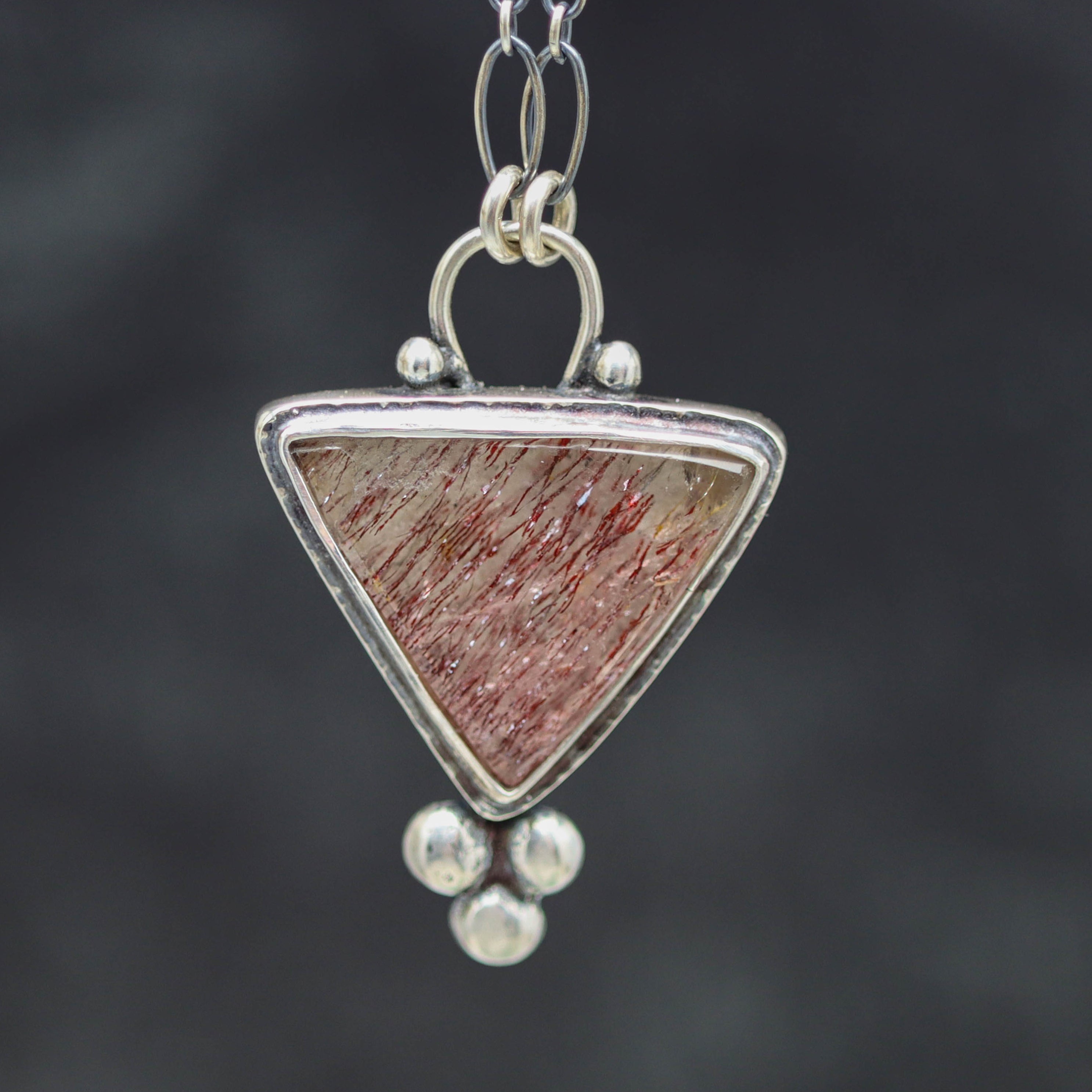 Necklace with a triangular pendant featuring a red and brown pattern on a dark background