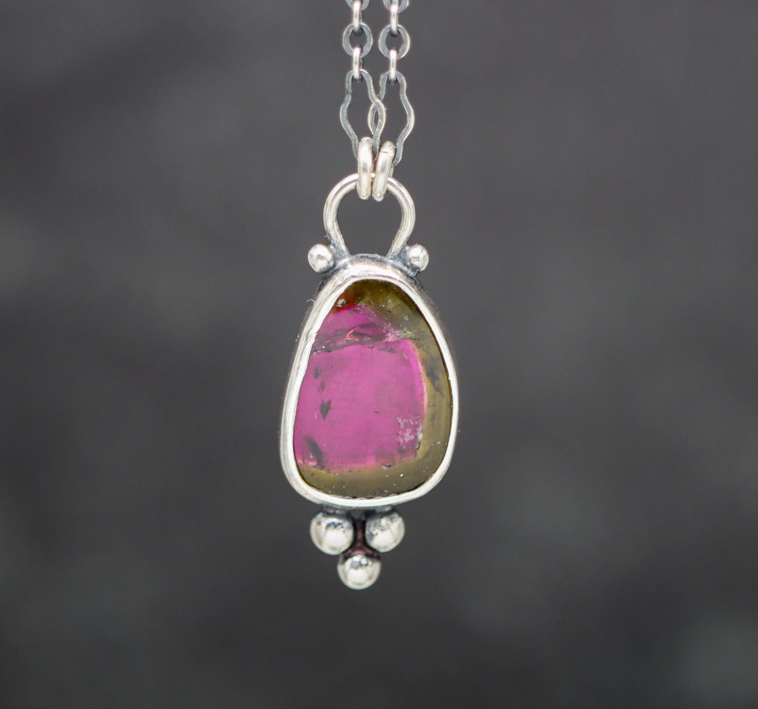 Silver pendant with a pink and green gemstone on a dark background