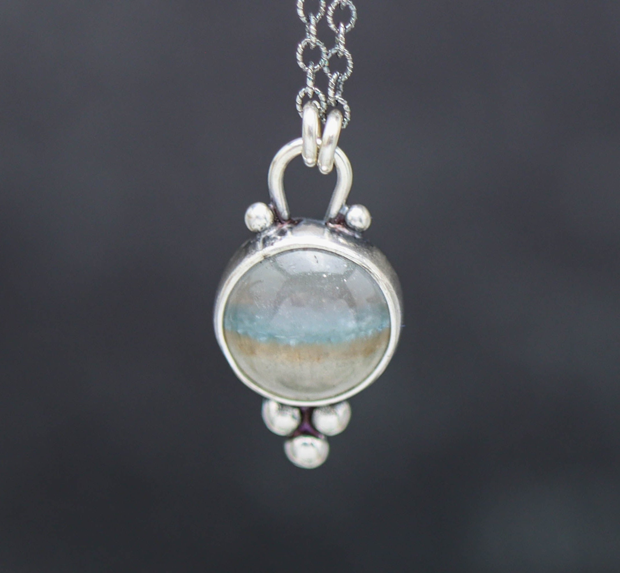 Silver pendant with a round stone on a dark background