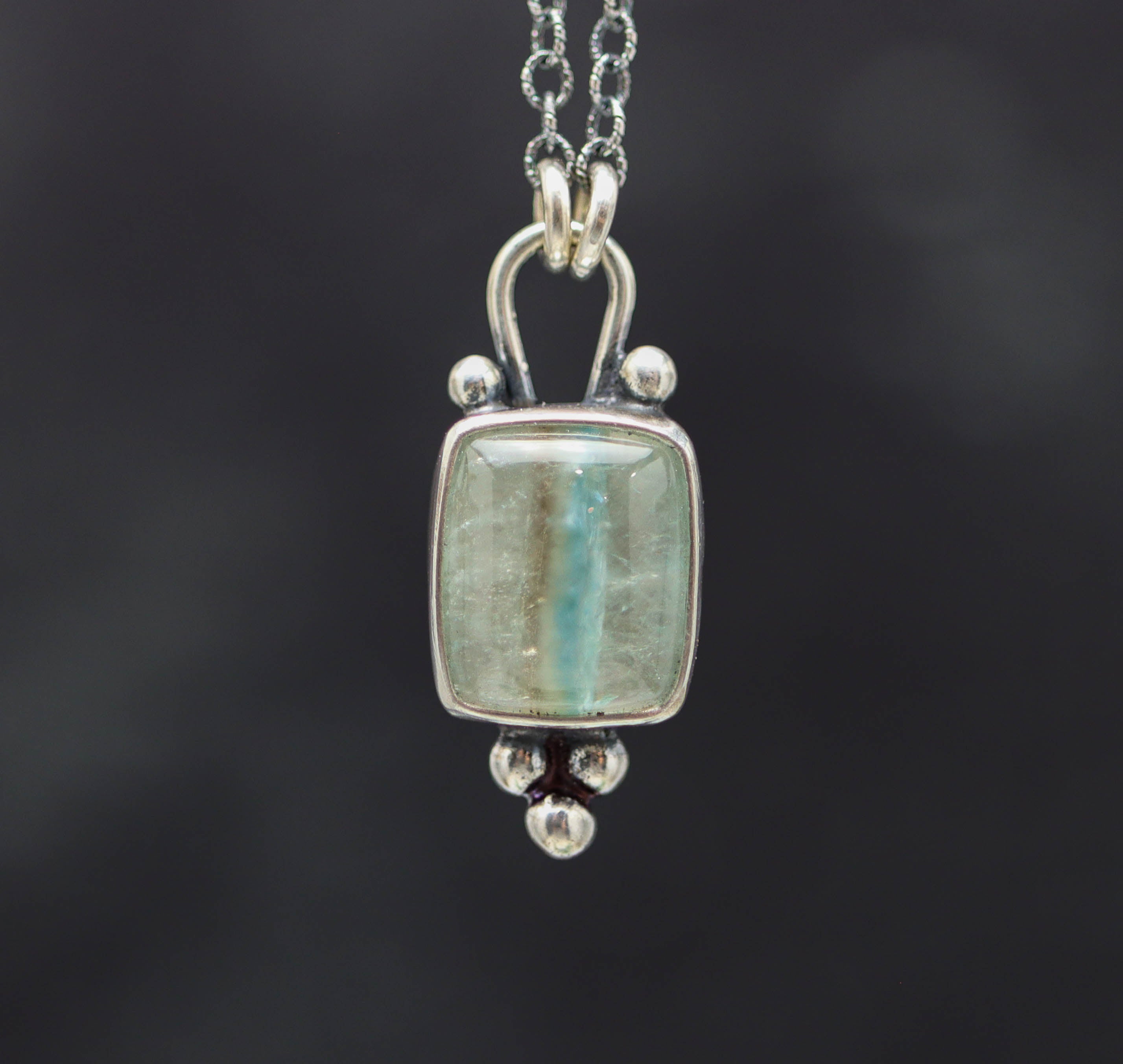 Silver pendant with a central gemstone on a dark background