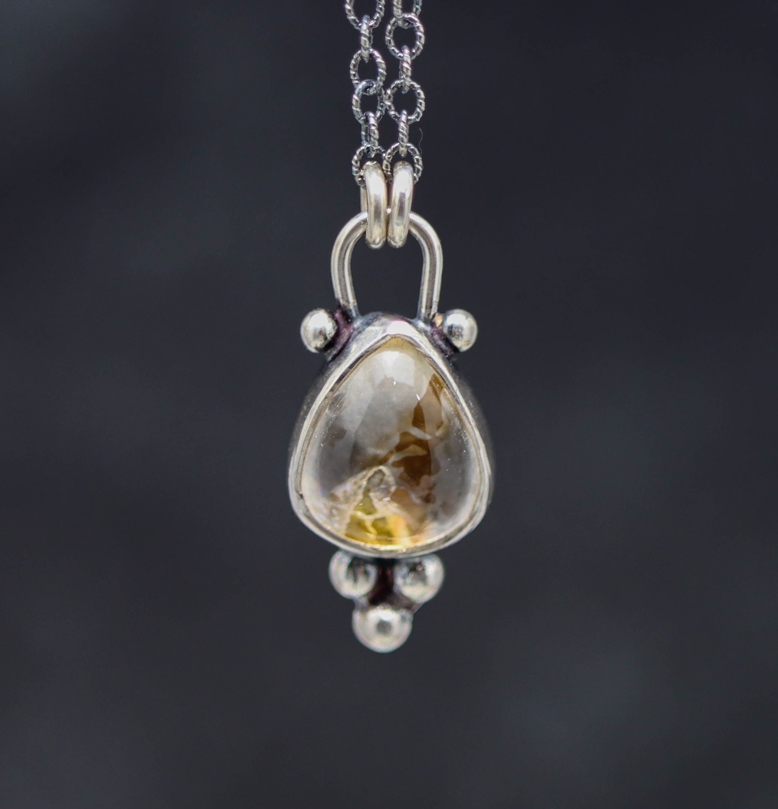 Silver pendant with a central gemstone on a dark background