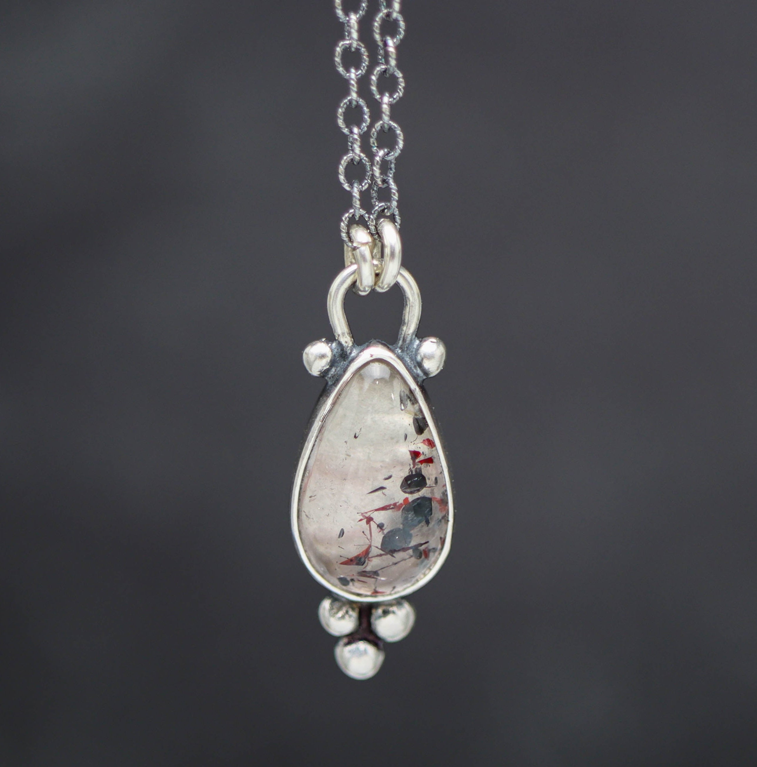 Teardrop-shaped pendant with a hematite in quartz on a chain against a dark background