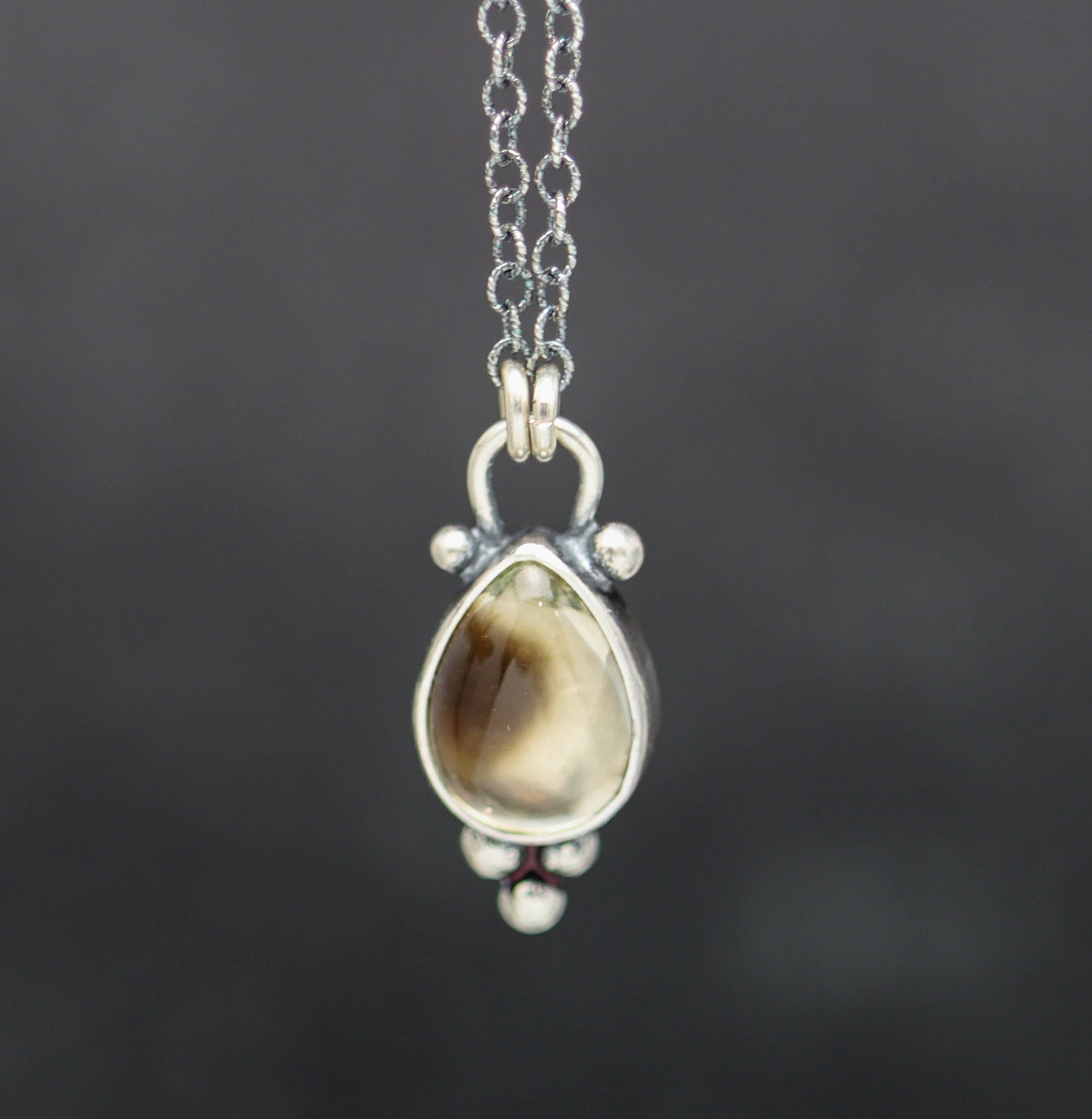 Teardrop-shaped pendant with a brown stone on a silver chain against a dark background