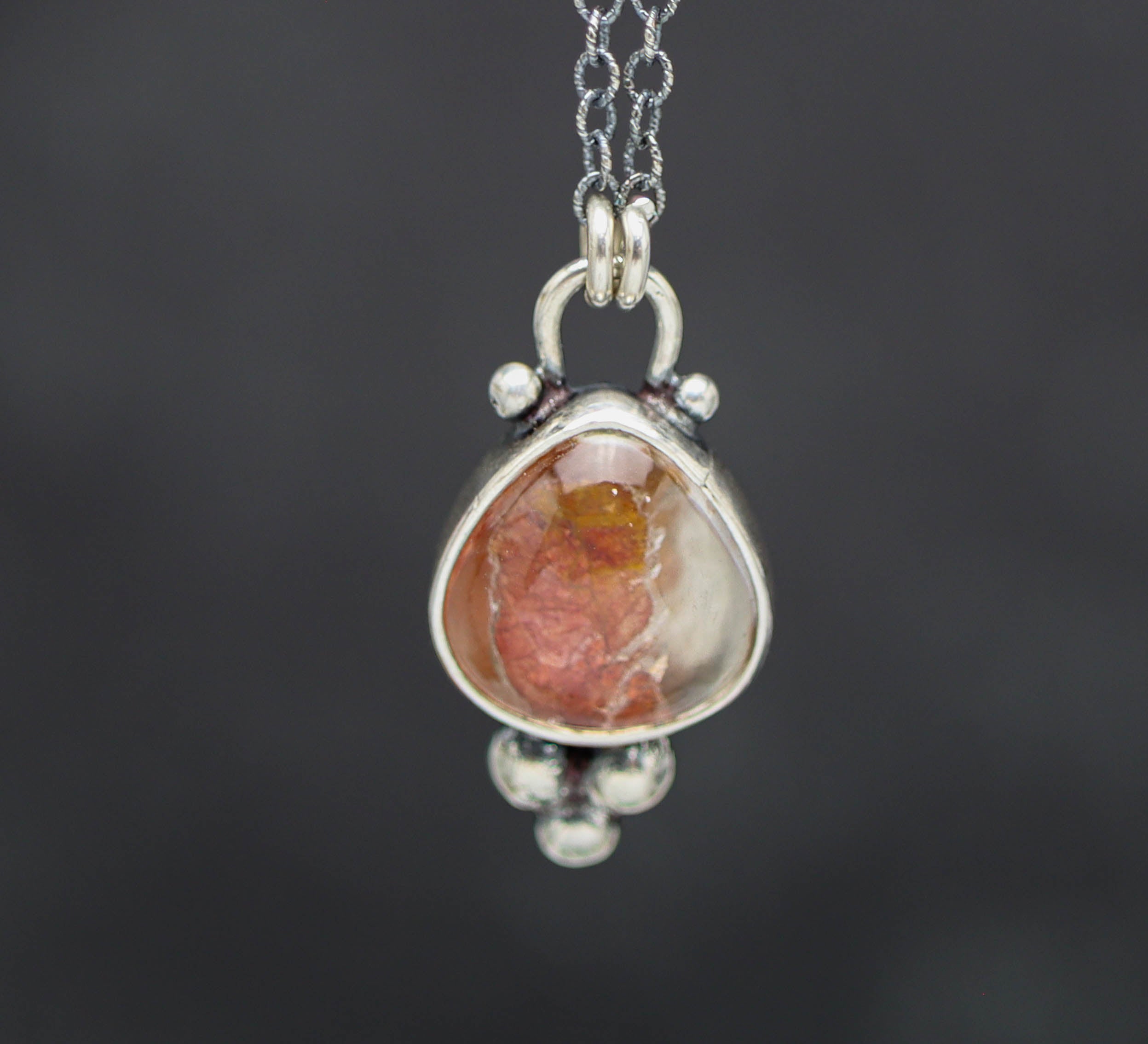 Silver pendant with a teardrop-shaped gemstone on a dark background