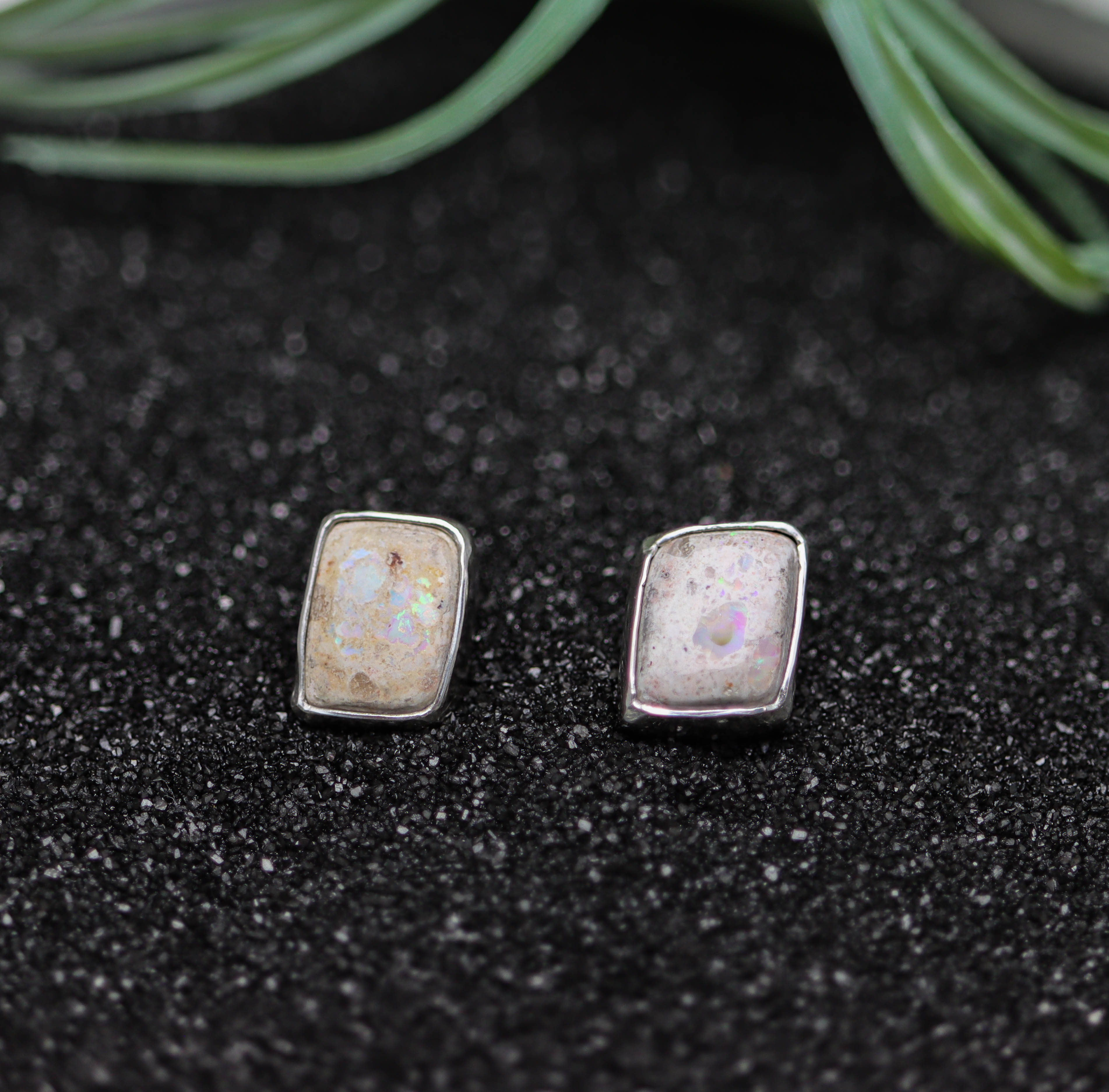 Pair of silver earrings with a natural stone design on a black textured surface.