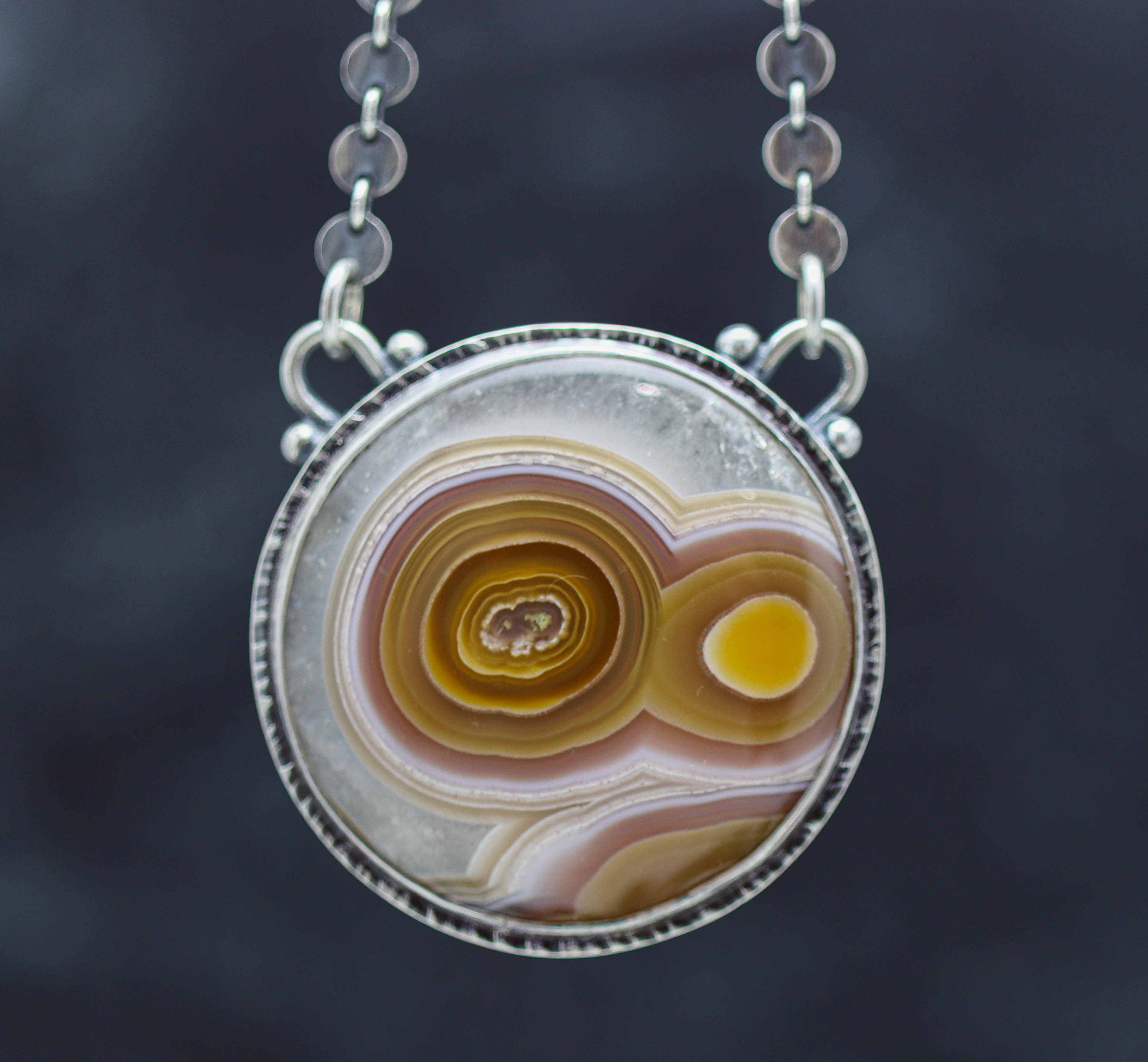 Necklace with a circular pendant featuring concentric color patterns on a dark background