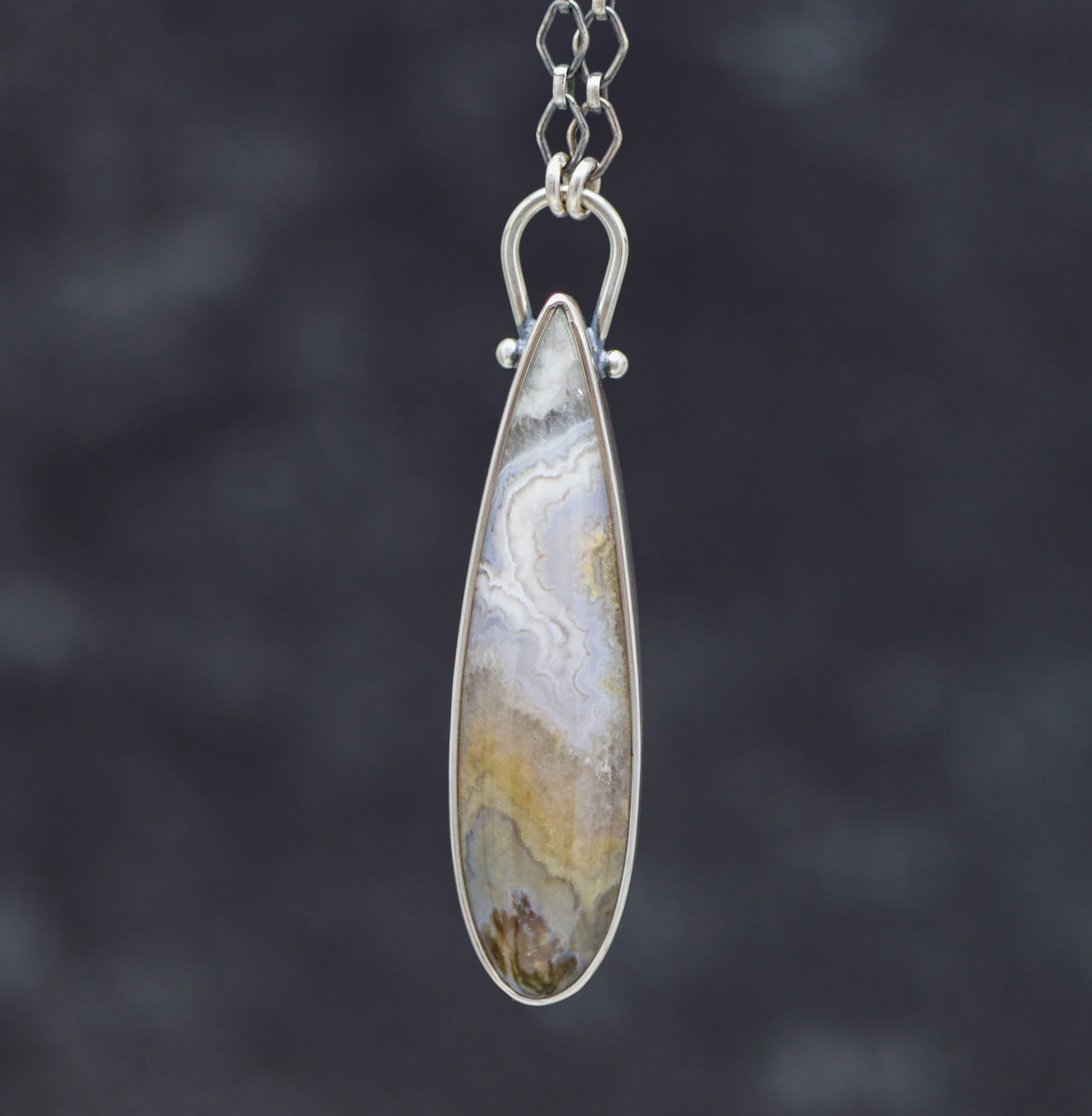 Teardrop-shaped pendant with a patterned stone on a dark background