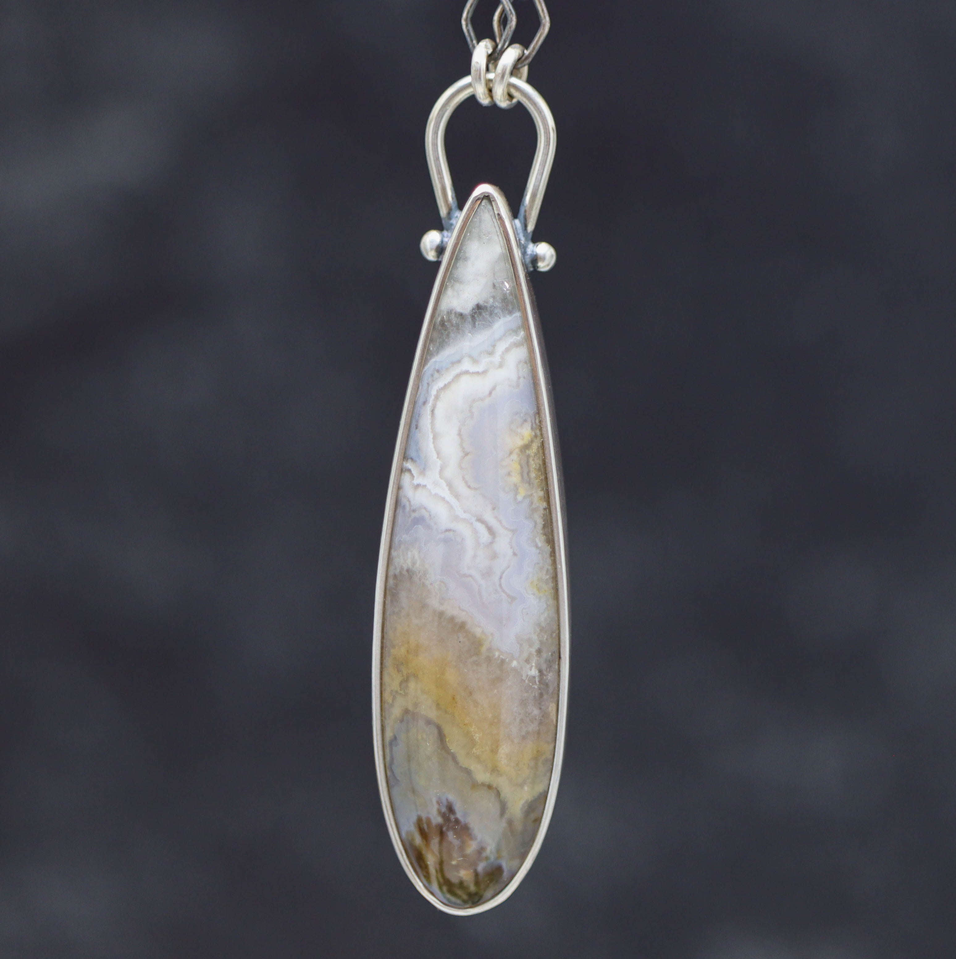 Teardrop-shaped pendant with a patterned stone on a dark background