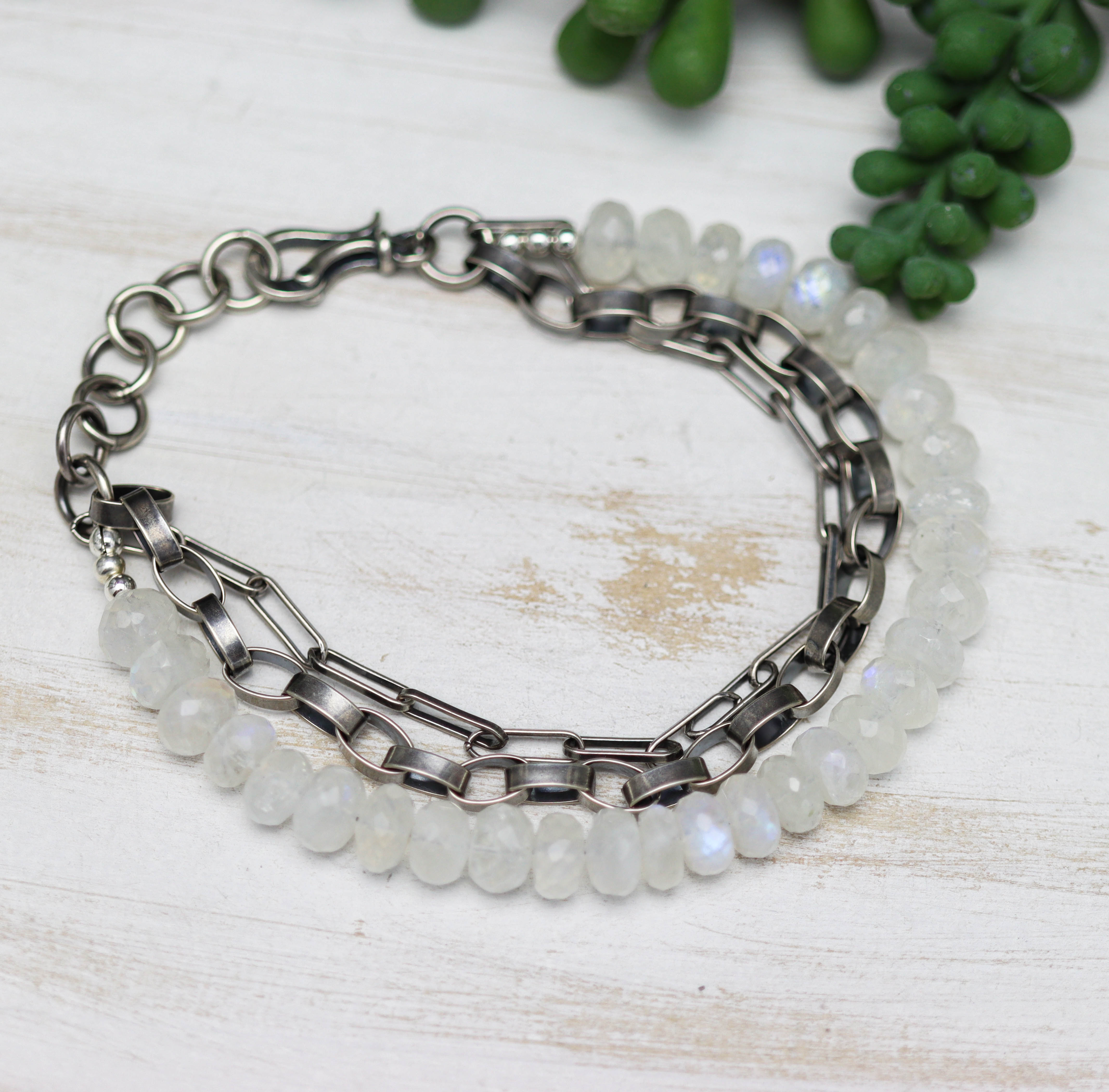 Bracelet with silver chain and beaded design on a light wooden surface with greenery.