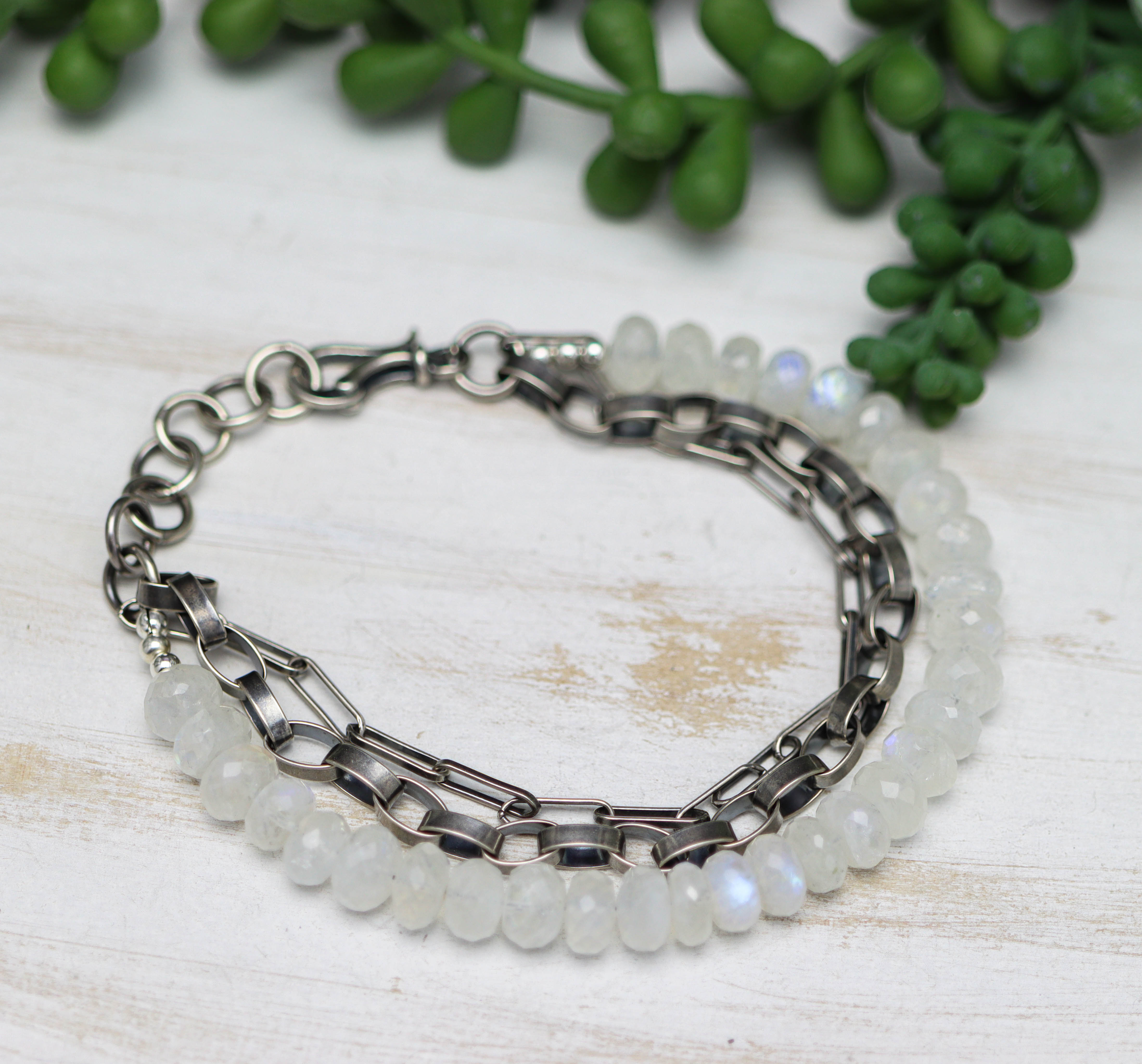 Bracelet with silver chain and white beads on a light wooden surface with greenery.