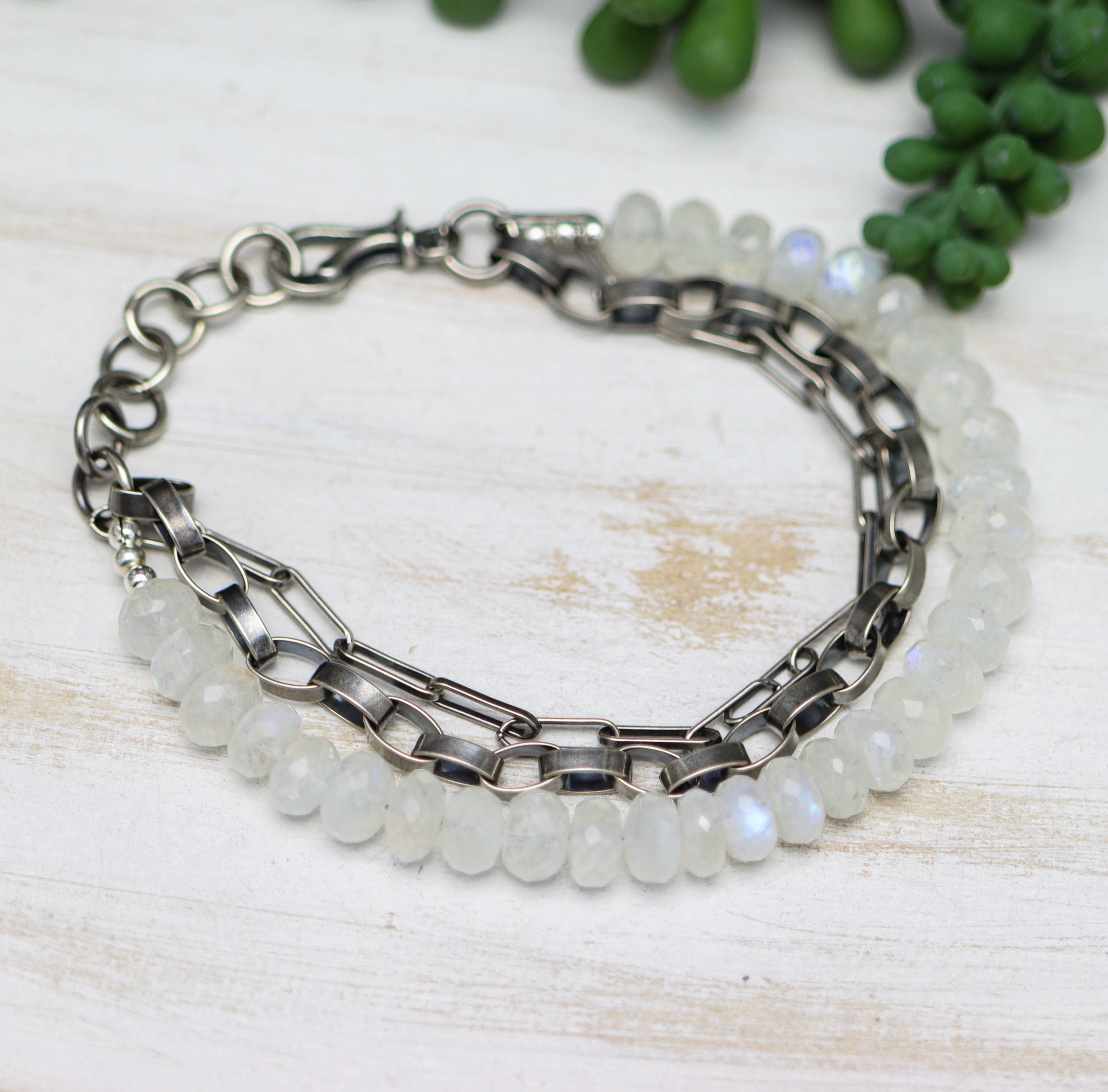 Bracelet with silver chain and white beads on a light wooden surface with greenery.