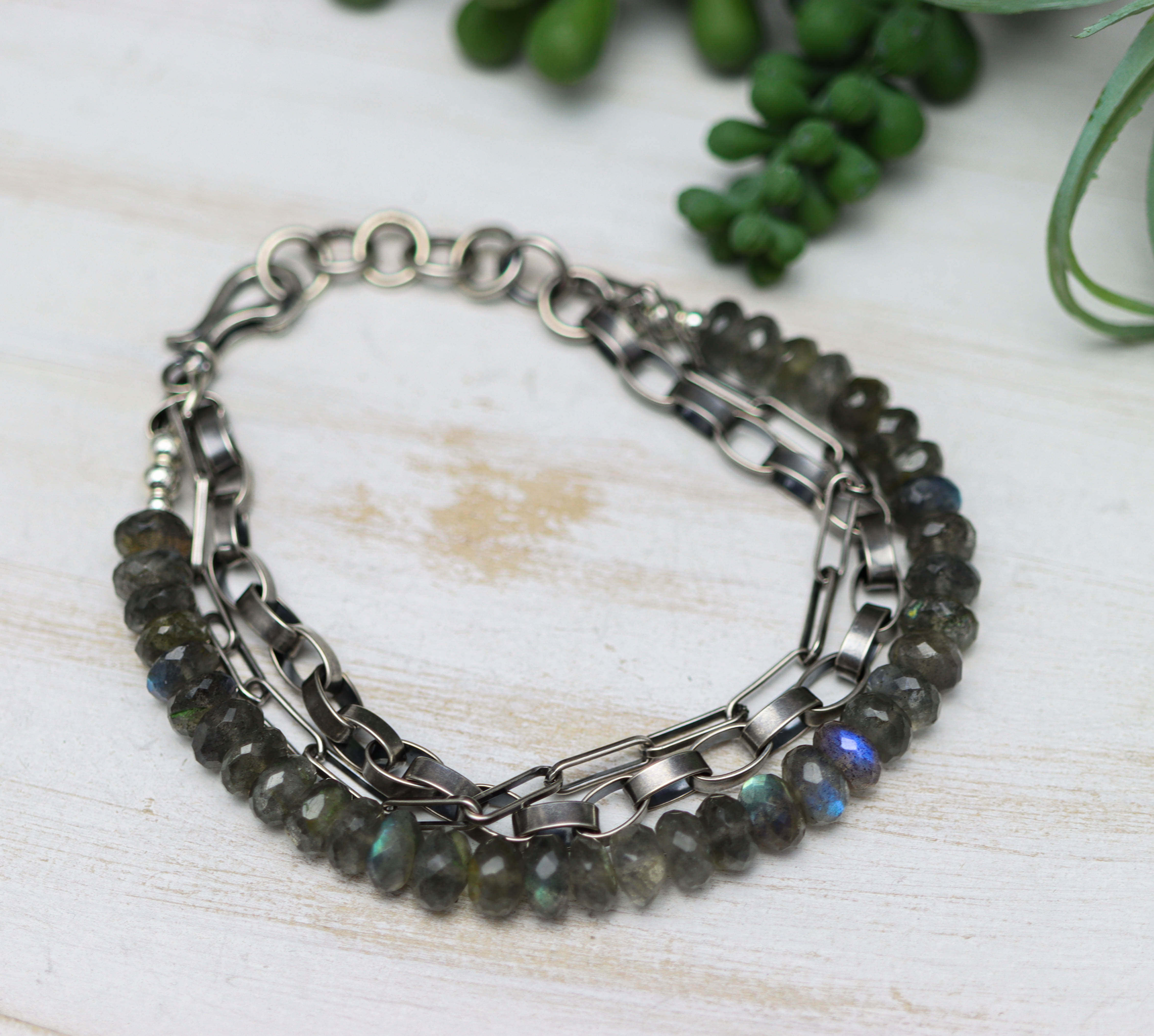 Stack of beaded bracelets on a light wooden surface with greenery in the background
