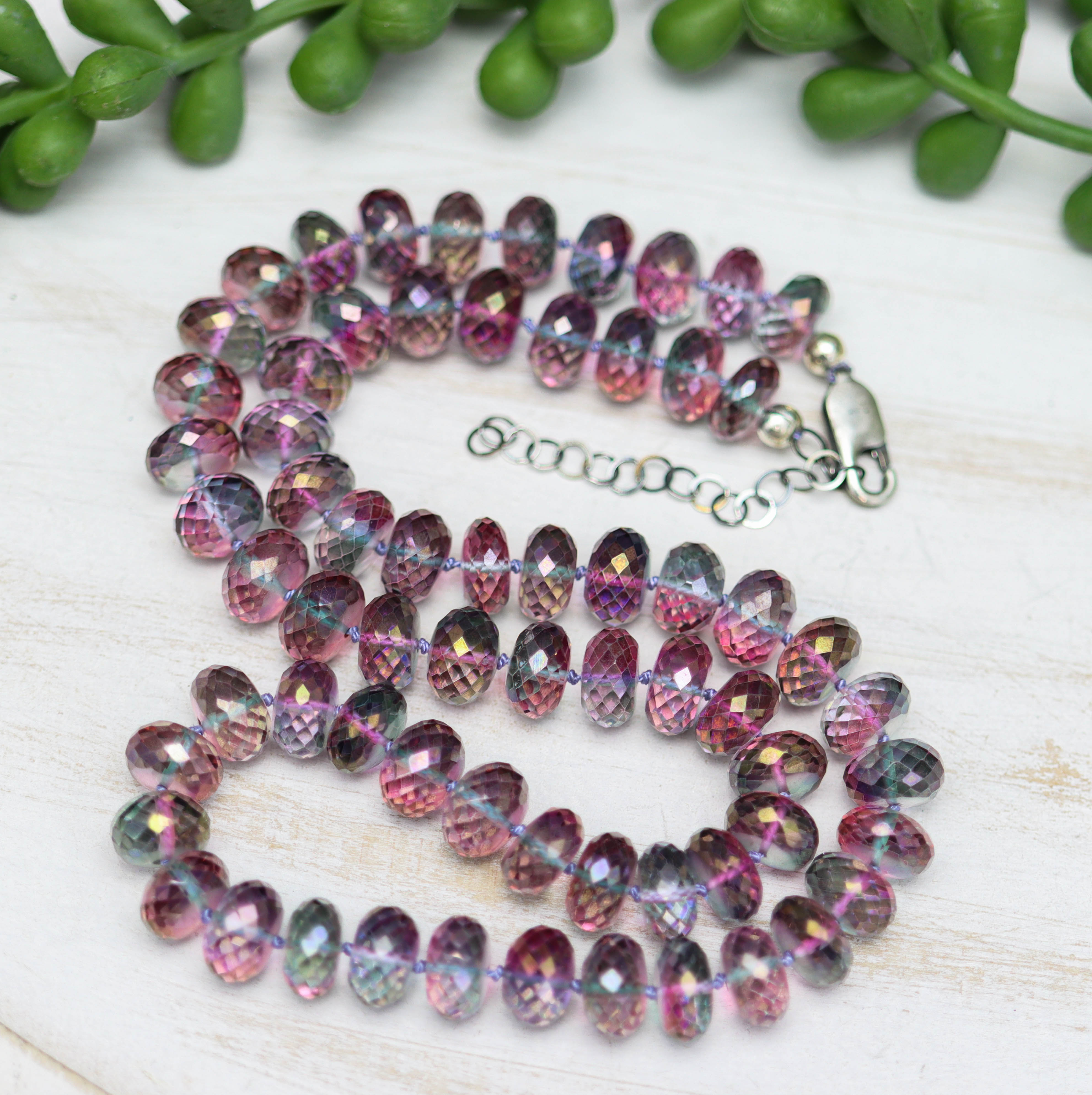 Multicolored beaded necklace on a light wooden surface with green leaves in the background