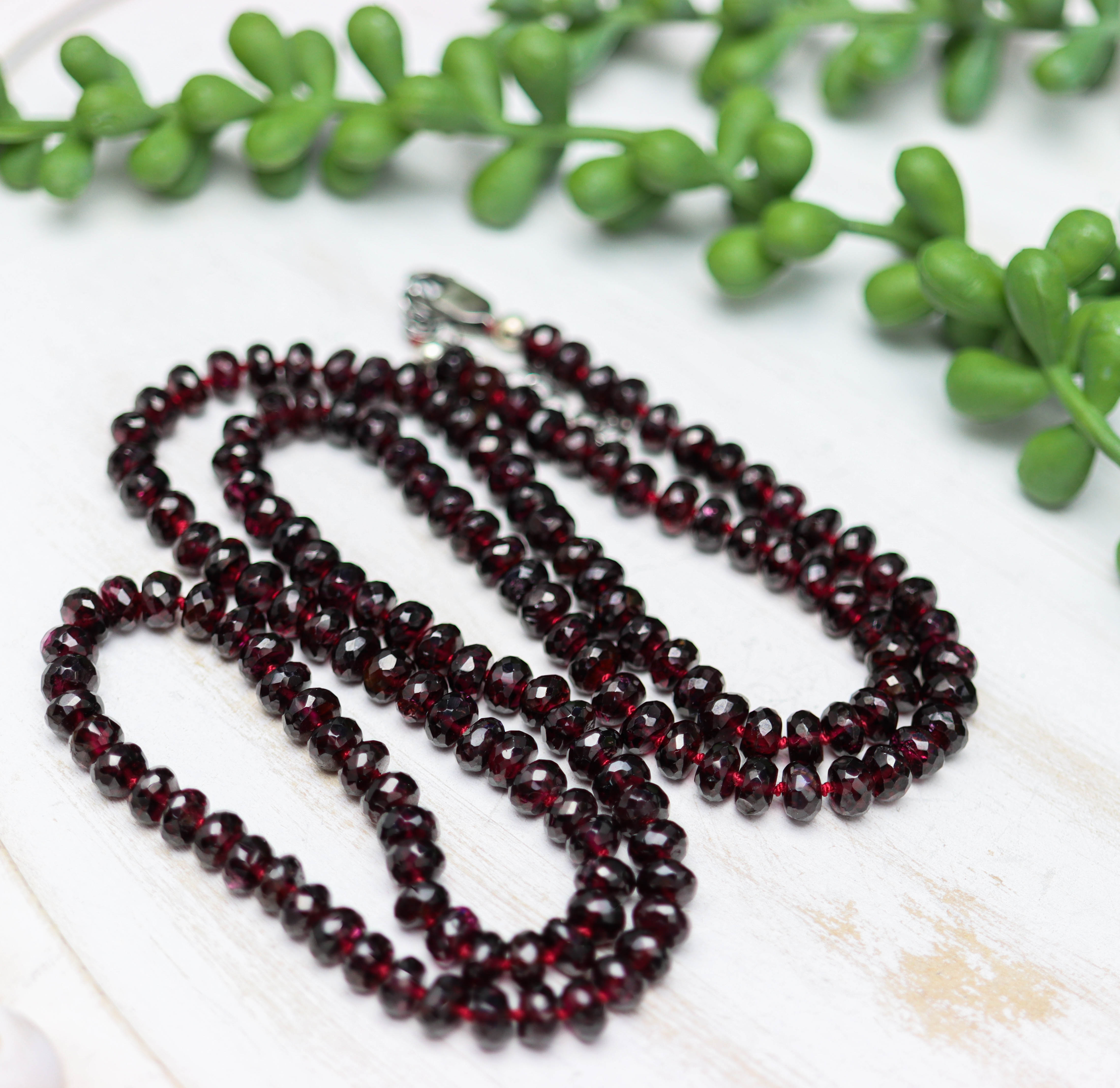 Garnet beaded necklace on a white surface with green leaves in the background