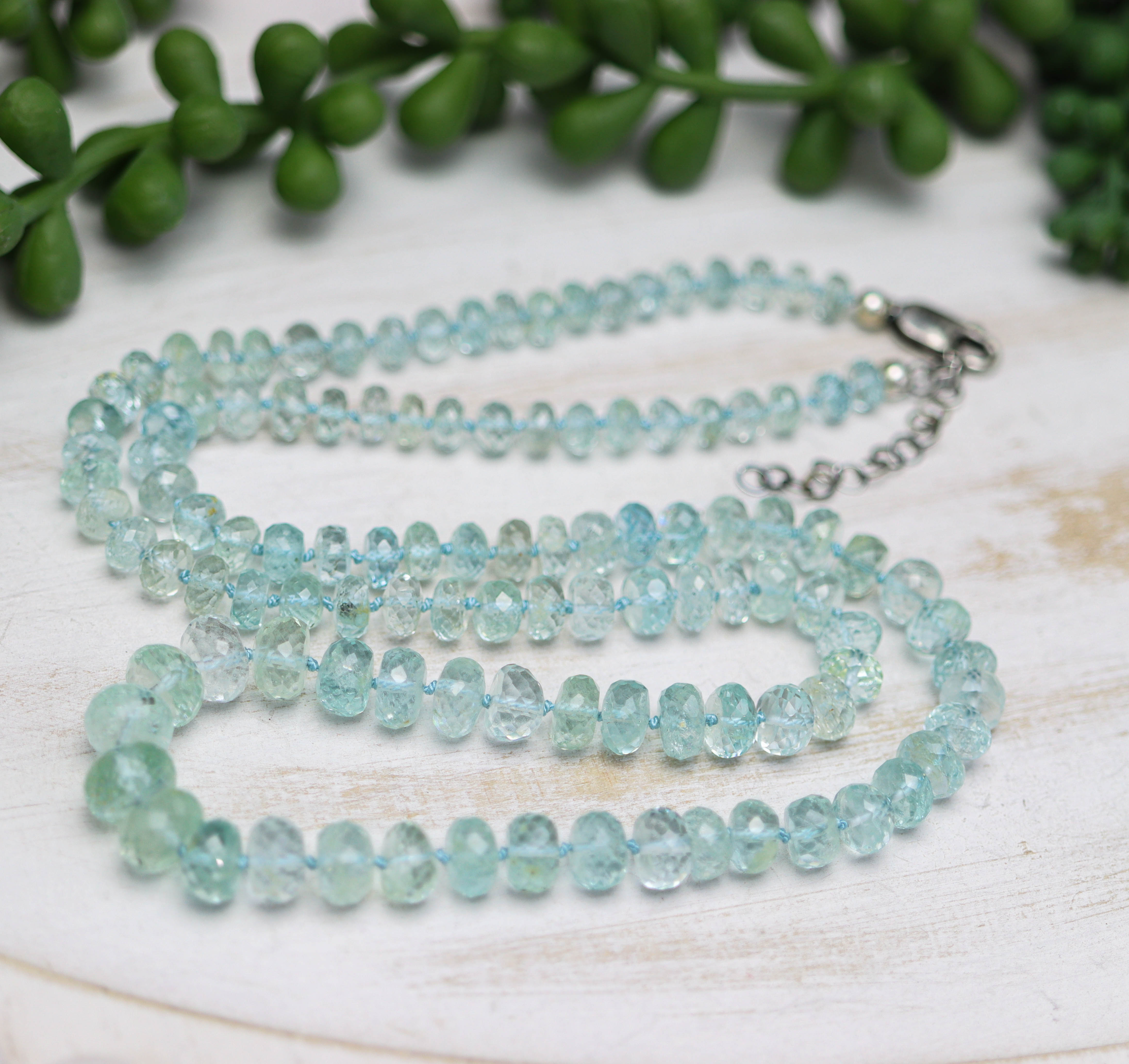 Necklace with light blue gemstones on a wooden surface with greenery in the background