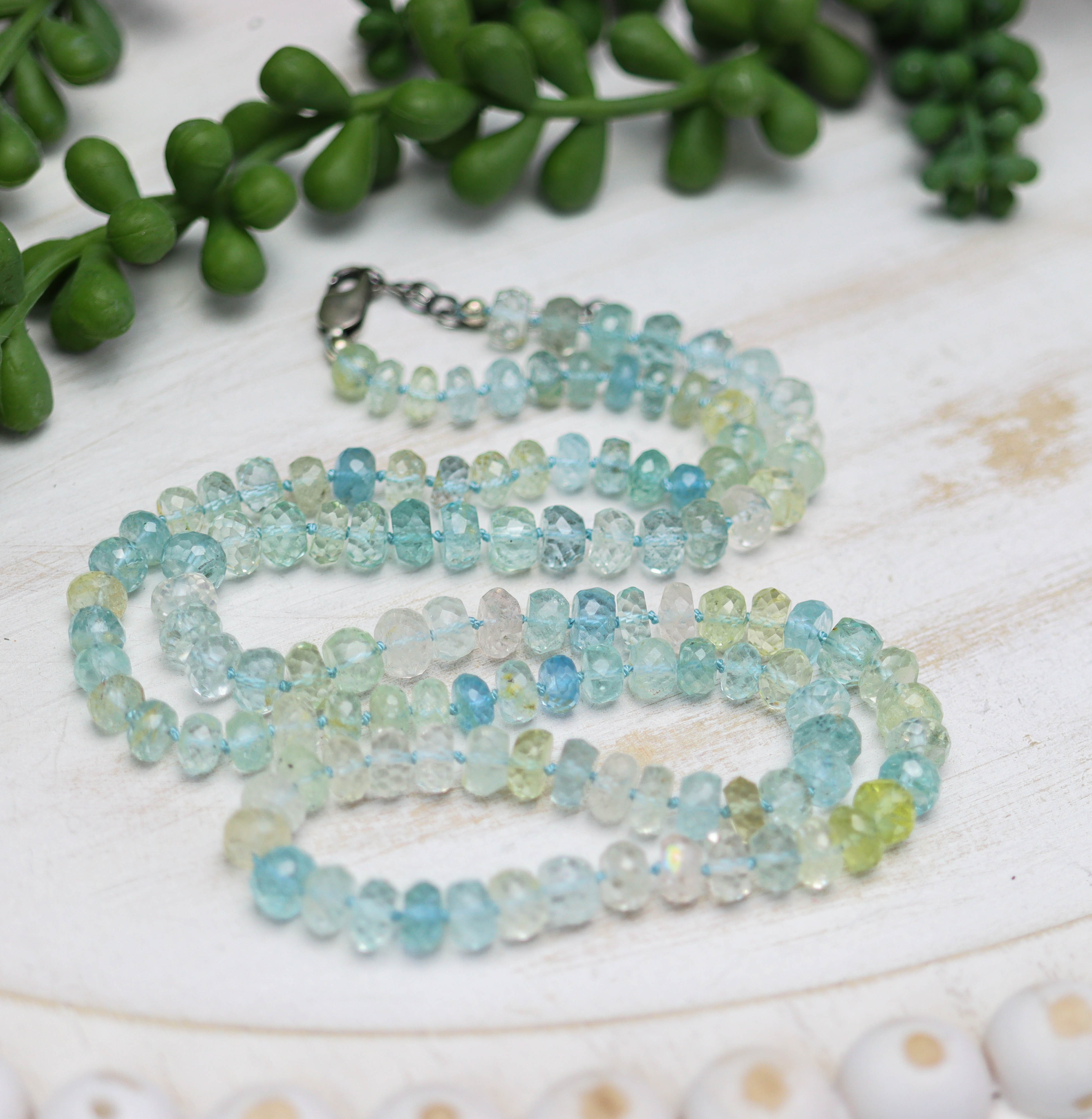 Beaded necklace with a silver clasp on a white surface with green leaves in the background