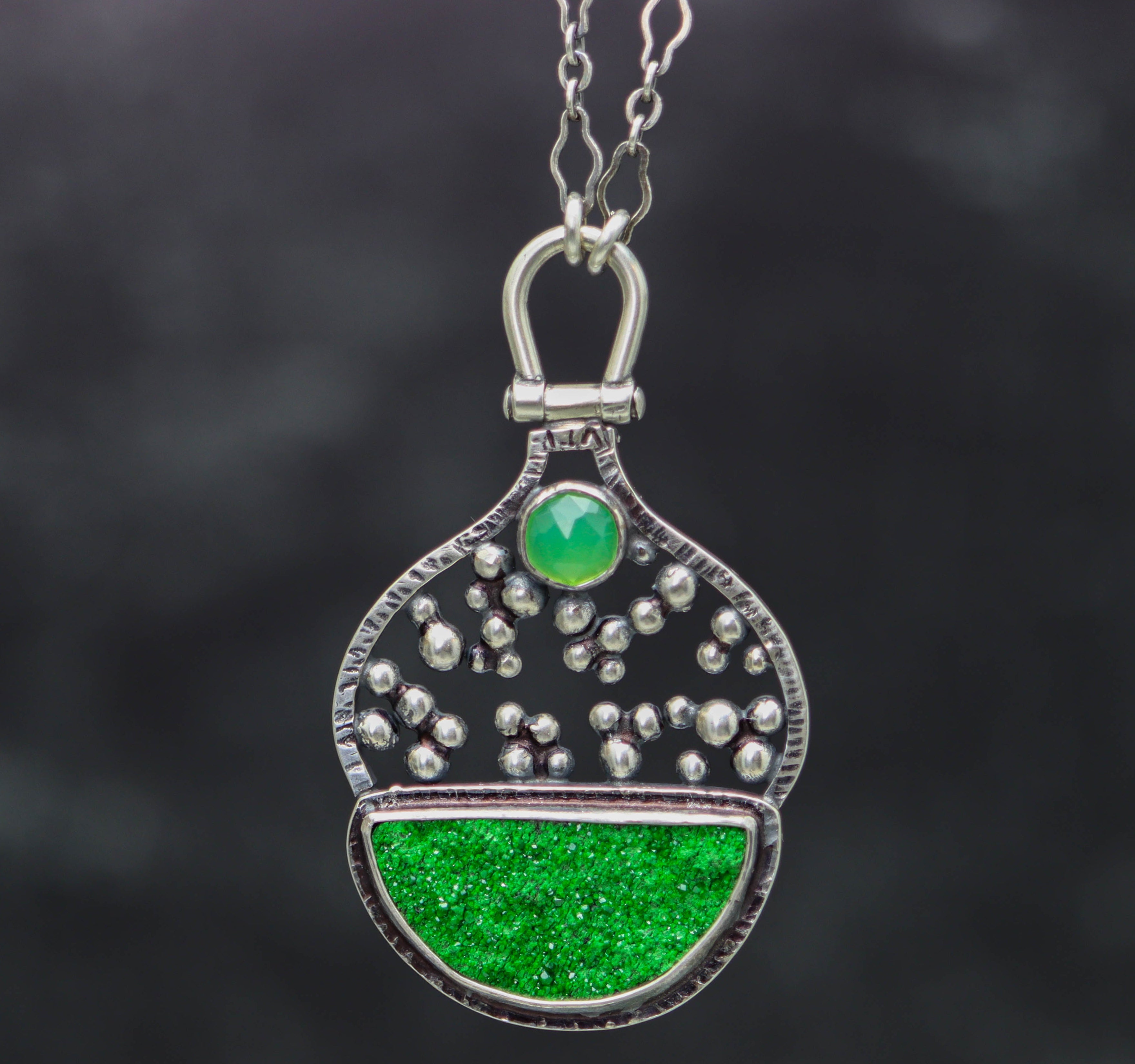 Green pendant necklace with silver accents on a dark background