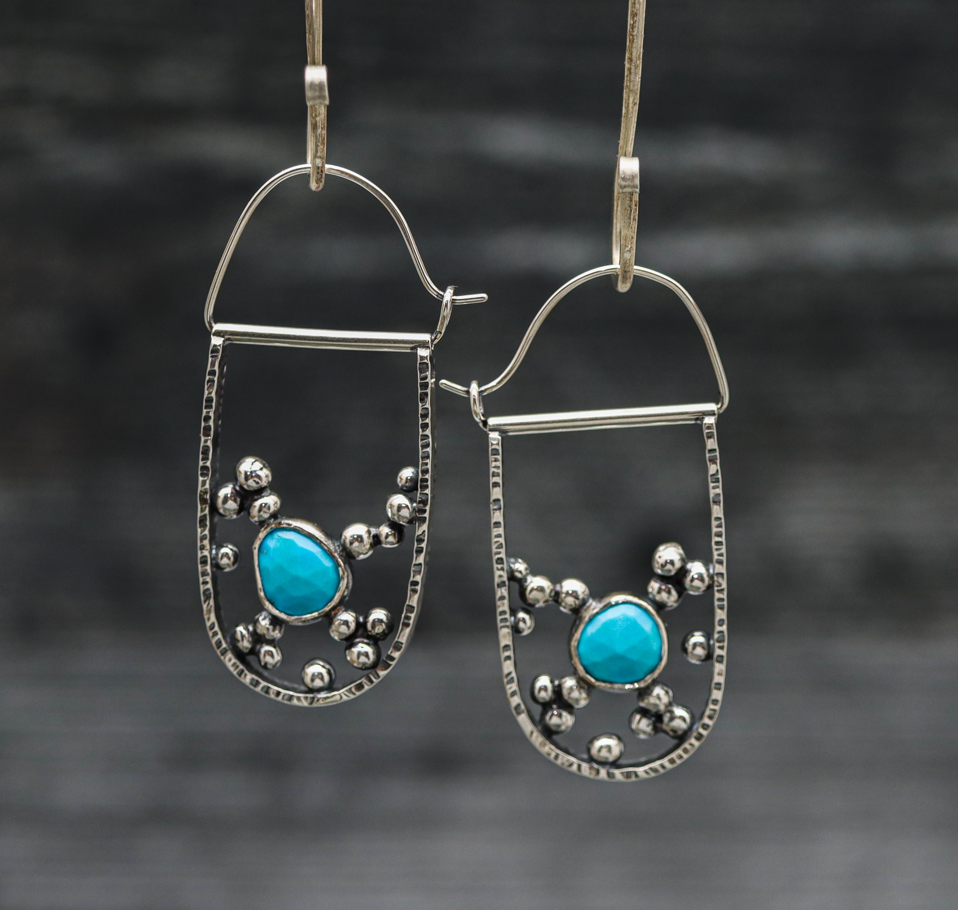 A pair of sterling silver hoop earrings with a central turquoise faceted rose cut and dangling silver beads.