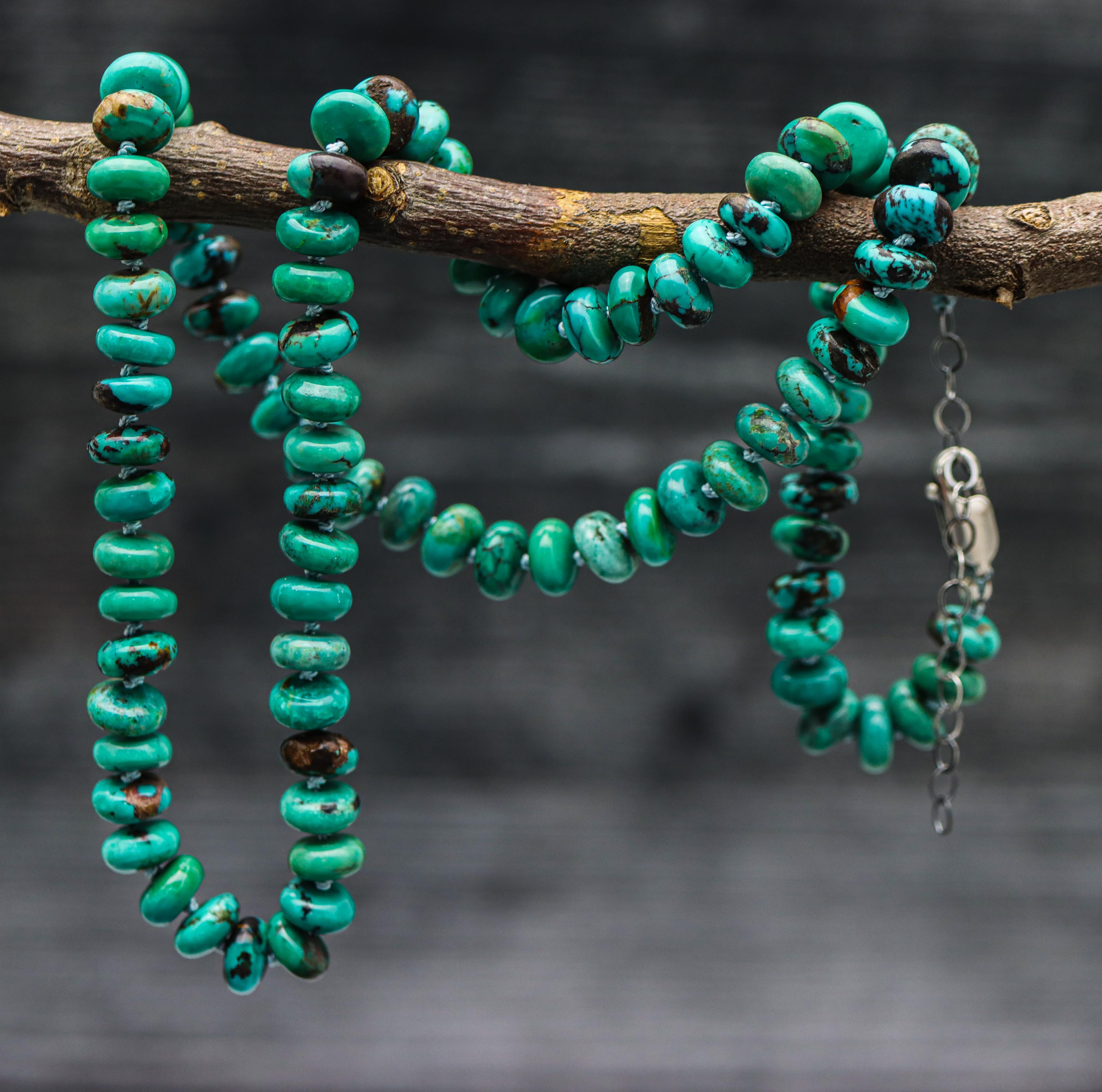 A turquoise hand knotted bead necklace with sterling silver closure, displayed on a silk thread against a dark background.