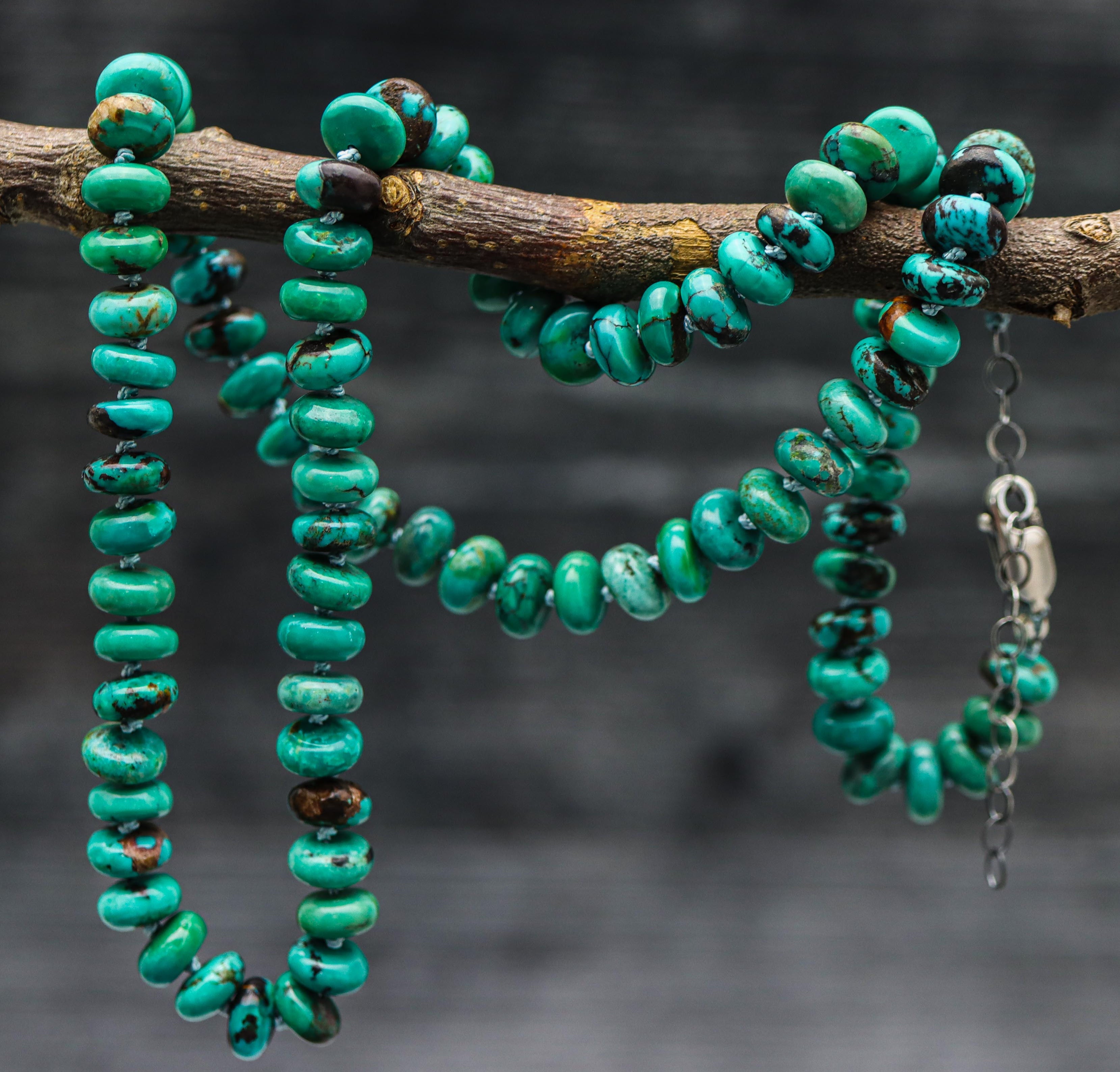 A turquoise hand knotted bead necklace with sterling silver closure, displayed on a silk thread against a dark background.