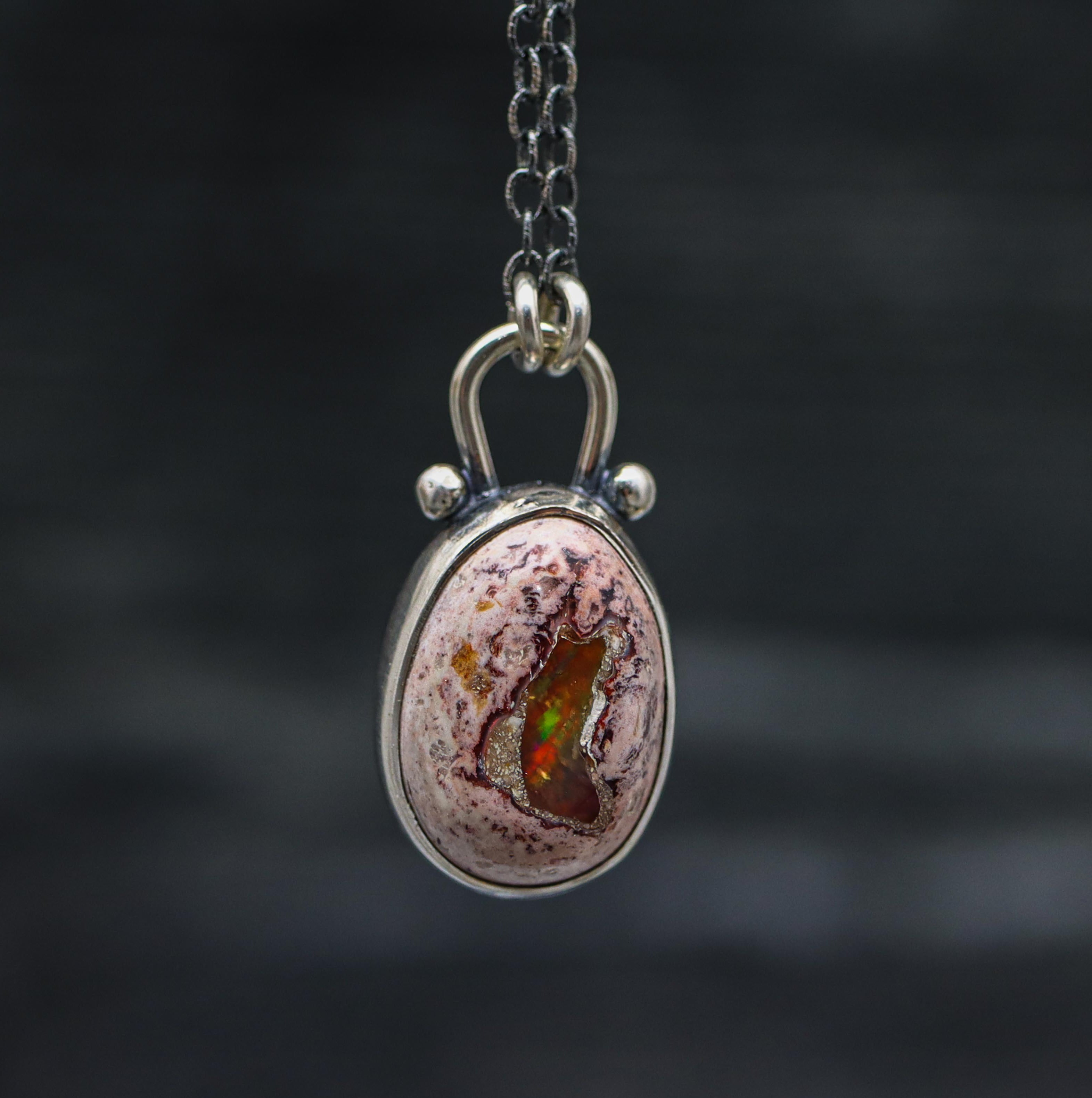 A sterling silver pendant necklace with a Mexican fire opal centerpiece featuring a rainbow flash, suspended from a silver chain.