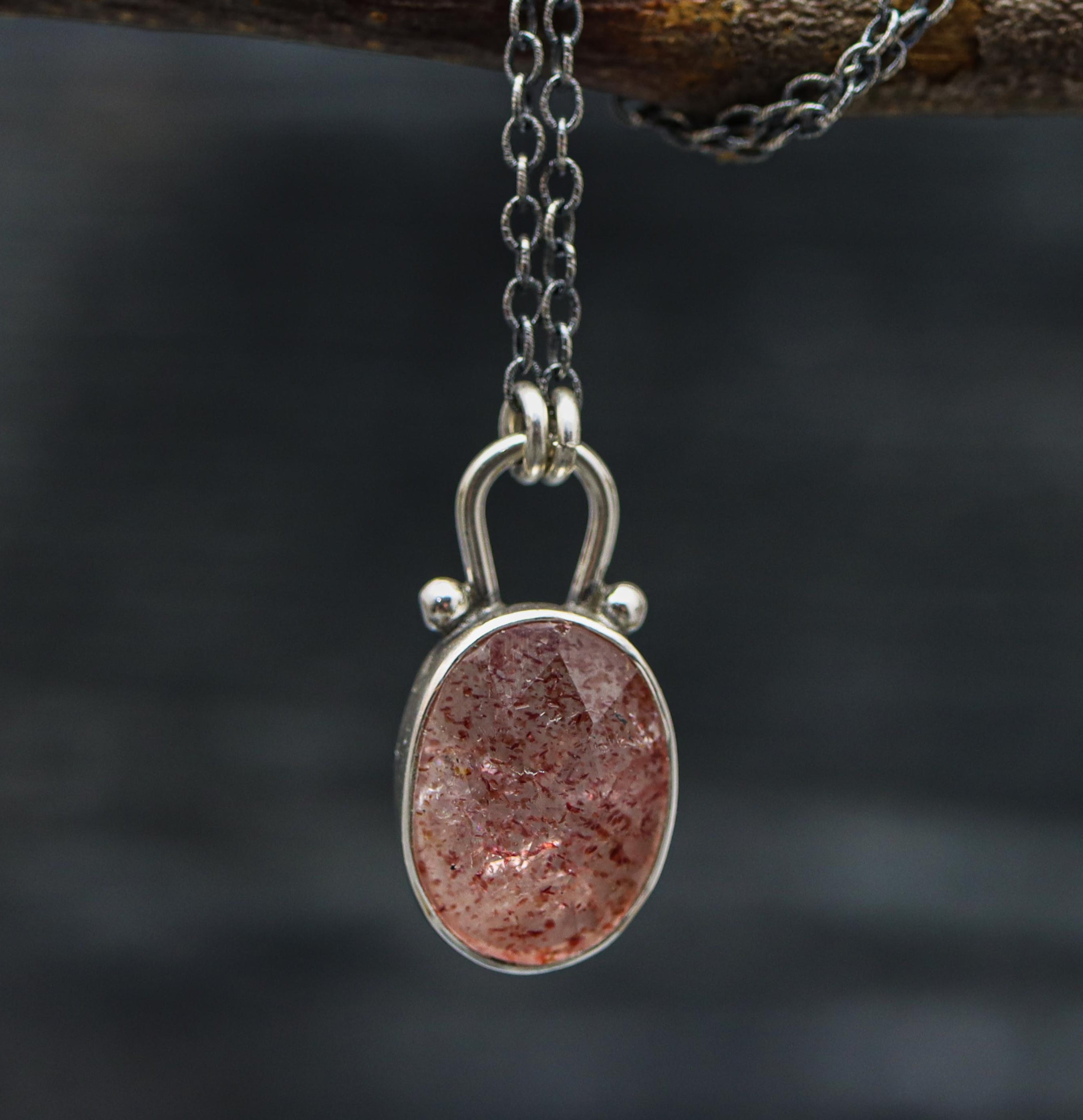 A sterling silver pendant necklace with a rose-cut strawberry quartz centerpiece, displayed on a branch against a dark background.