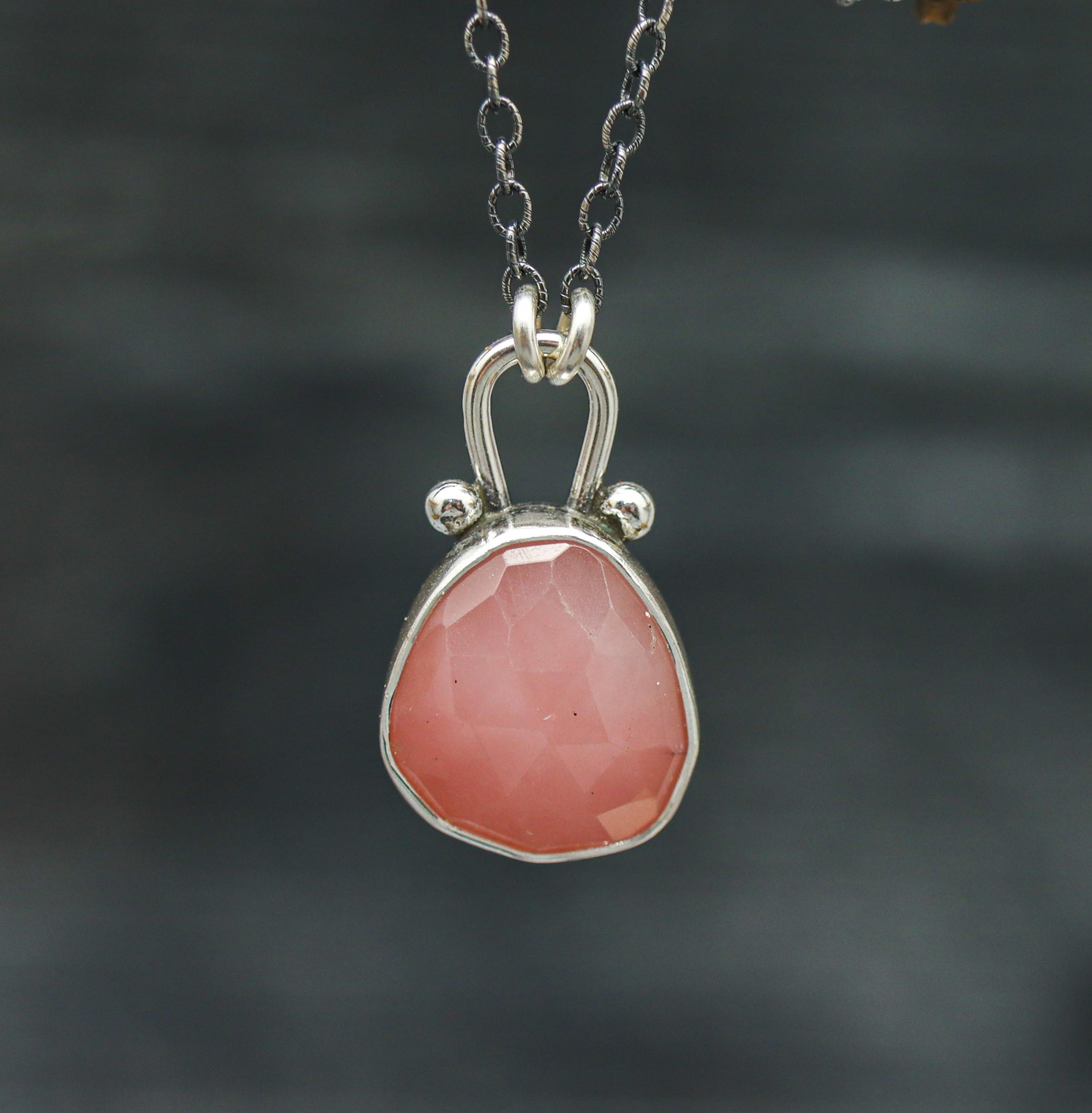 A sterling silver pendant necklace with a rose-cut pink guava quartz centerpiece, displayed on a silver chain against a natural background.