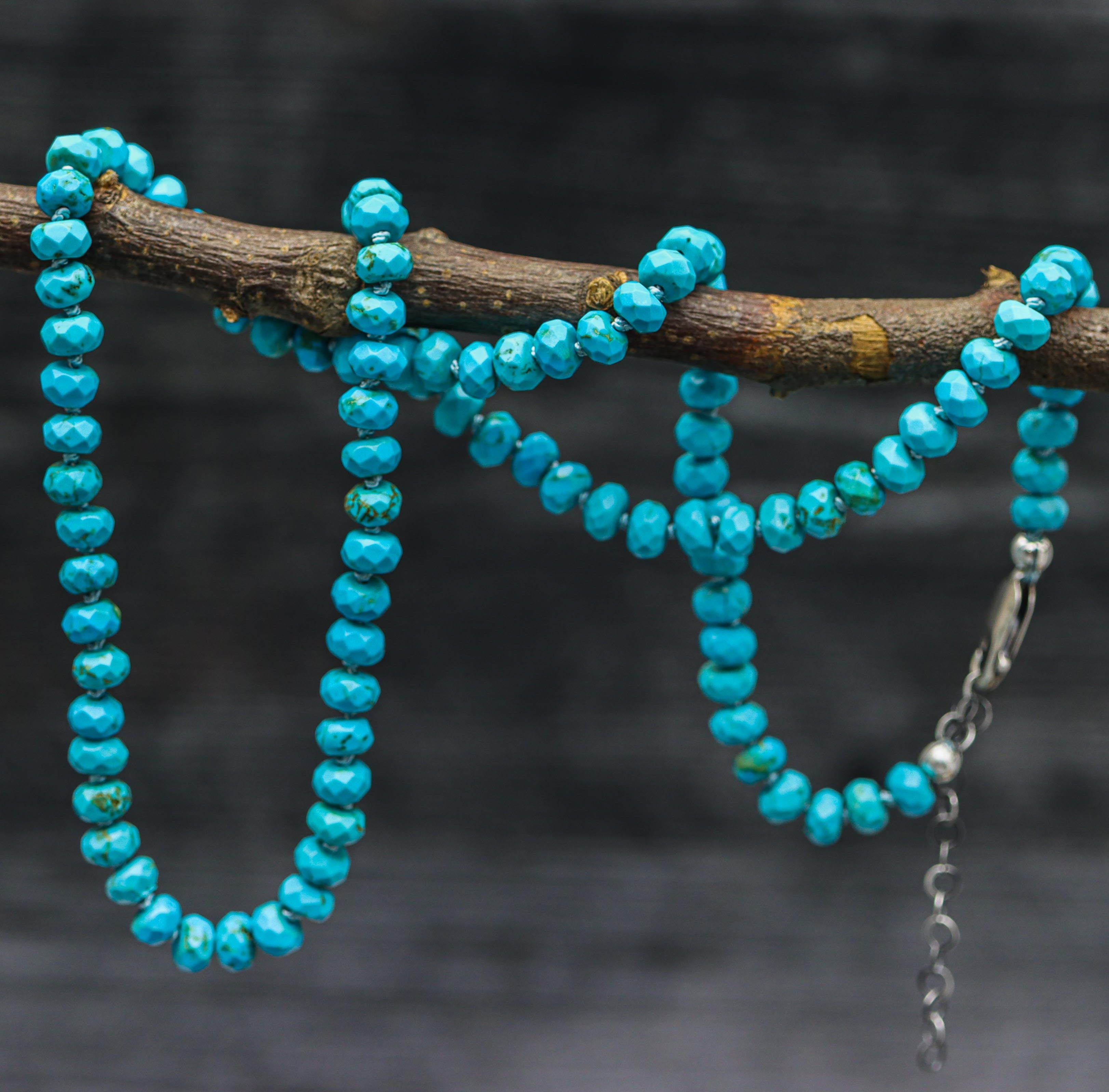 A turquoise hand-knotted bead necklace with sterling silver closure, displayed on a silk thread against a dark background.
