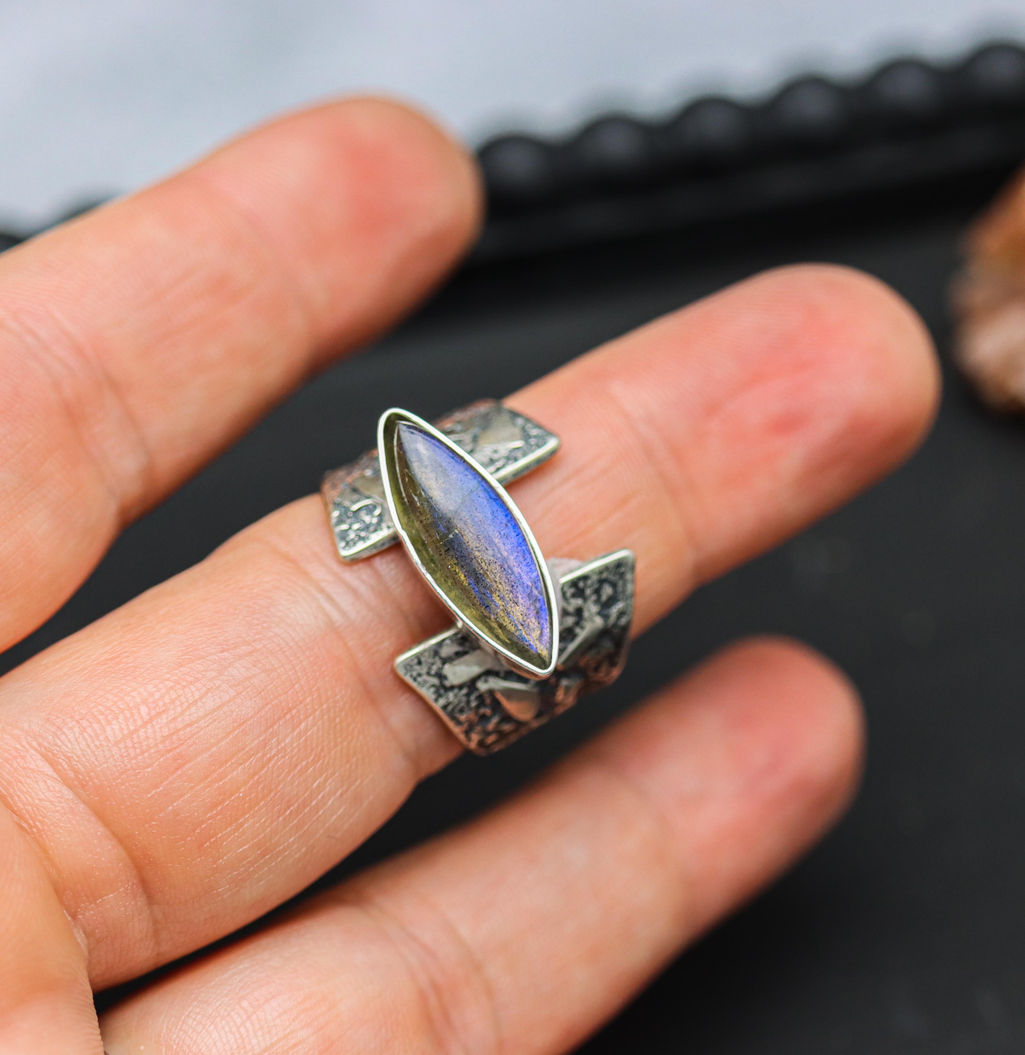 Ring with a labradorite stone set in a sterling silver setting, held on a person's finger.
