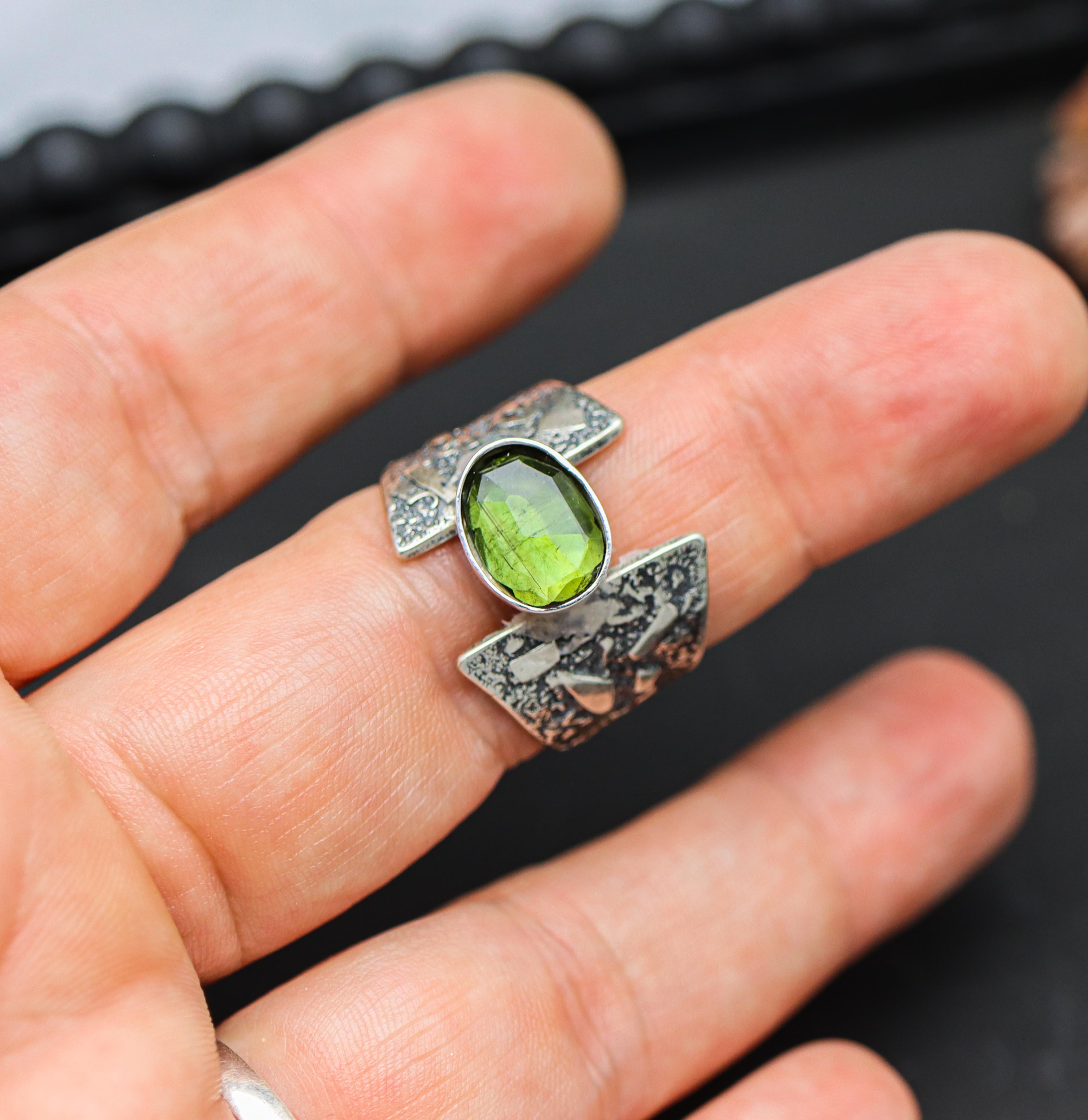 A hand holding a sterling silver ring with a green tourmaline gemstone, showcasing different band styles.