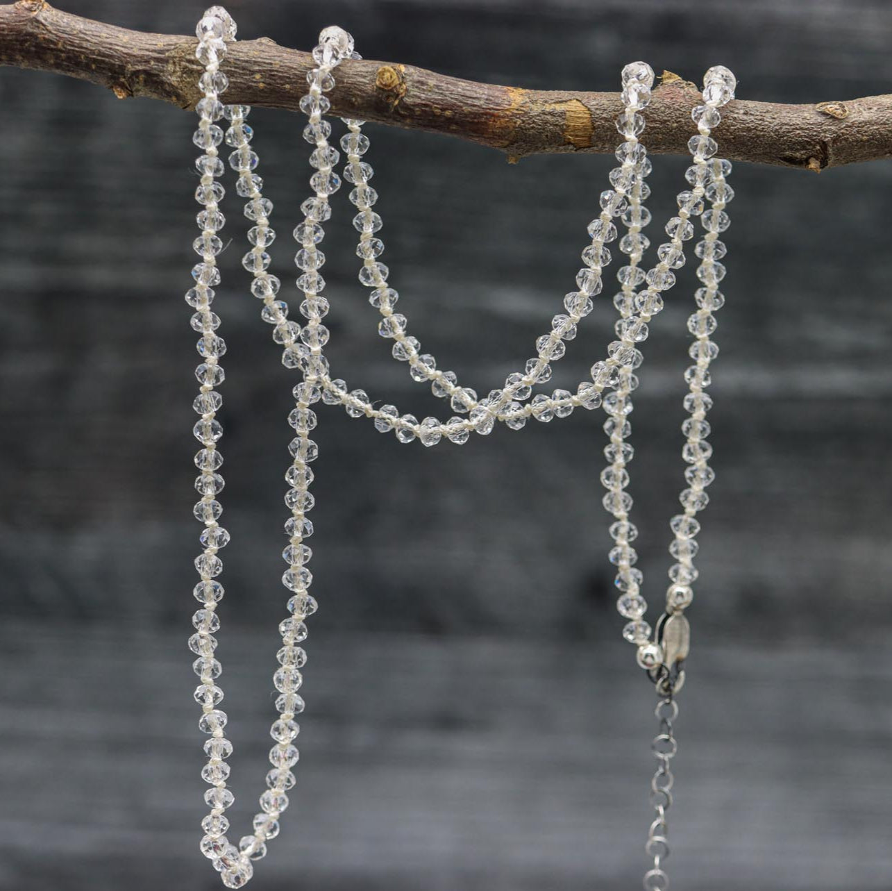 A hand knotted sterling silver necklace with clear crystal quartz beads, displayed on a branch.