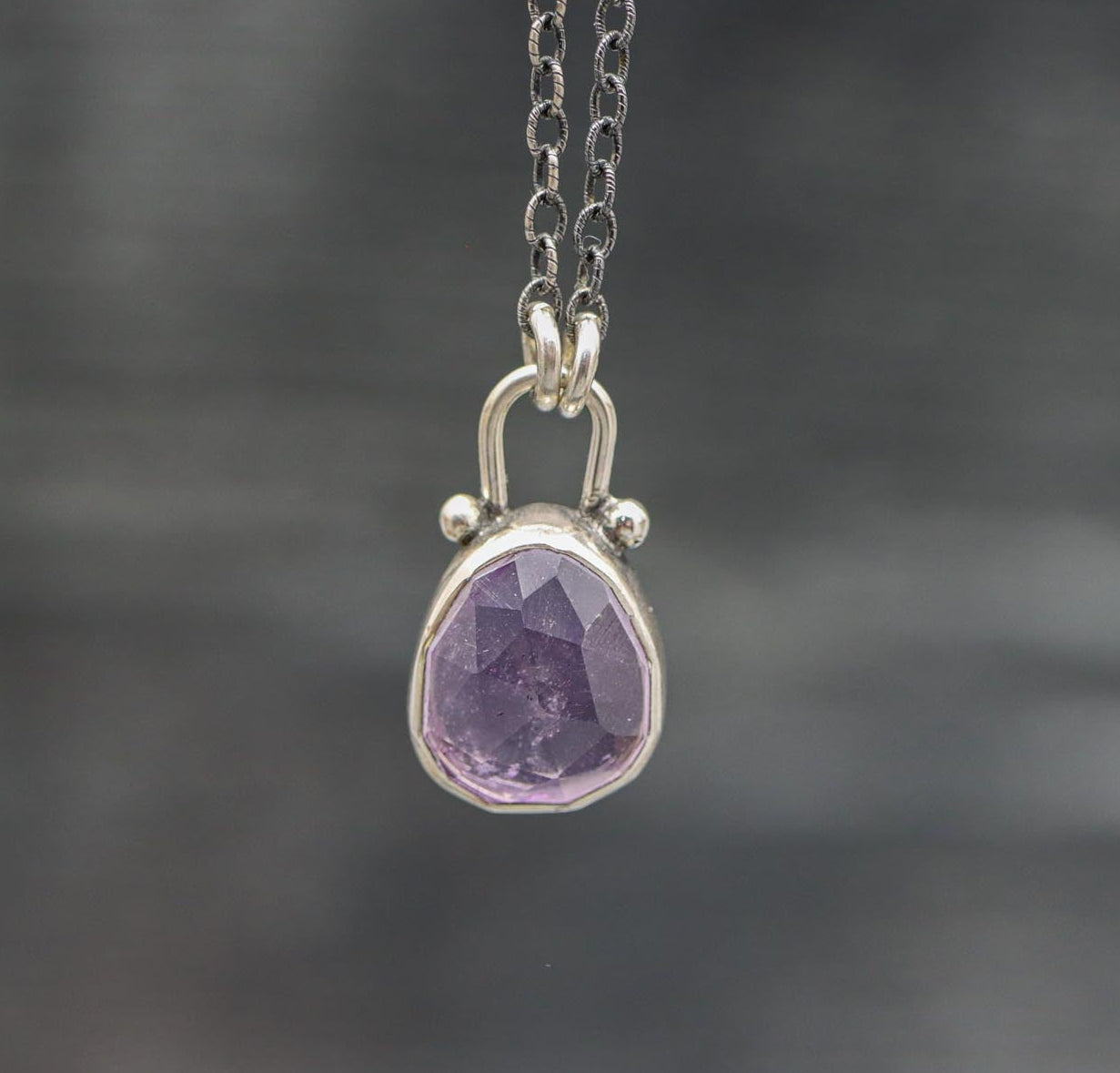 A sterling silver pendant necklace with a faceted rose cut amethyst centerpiece, suspended by a silver ball chain.