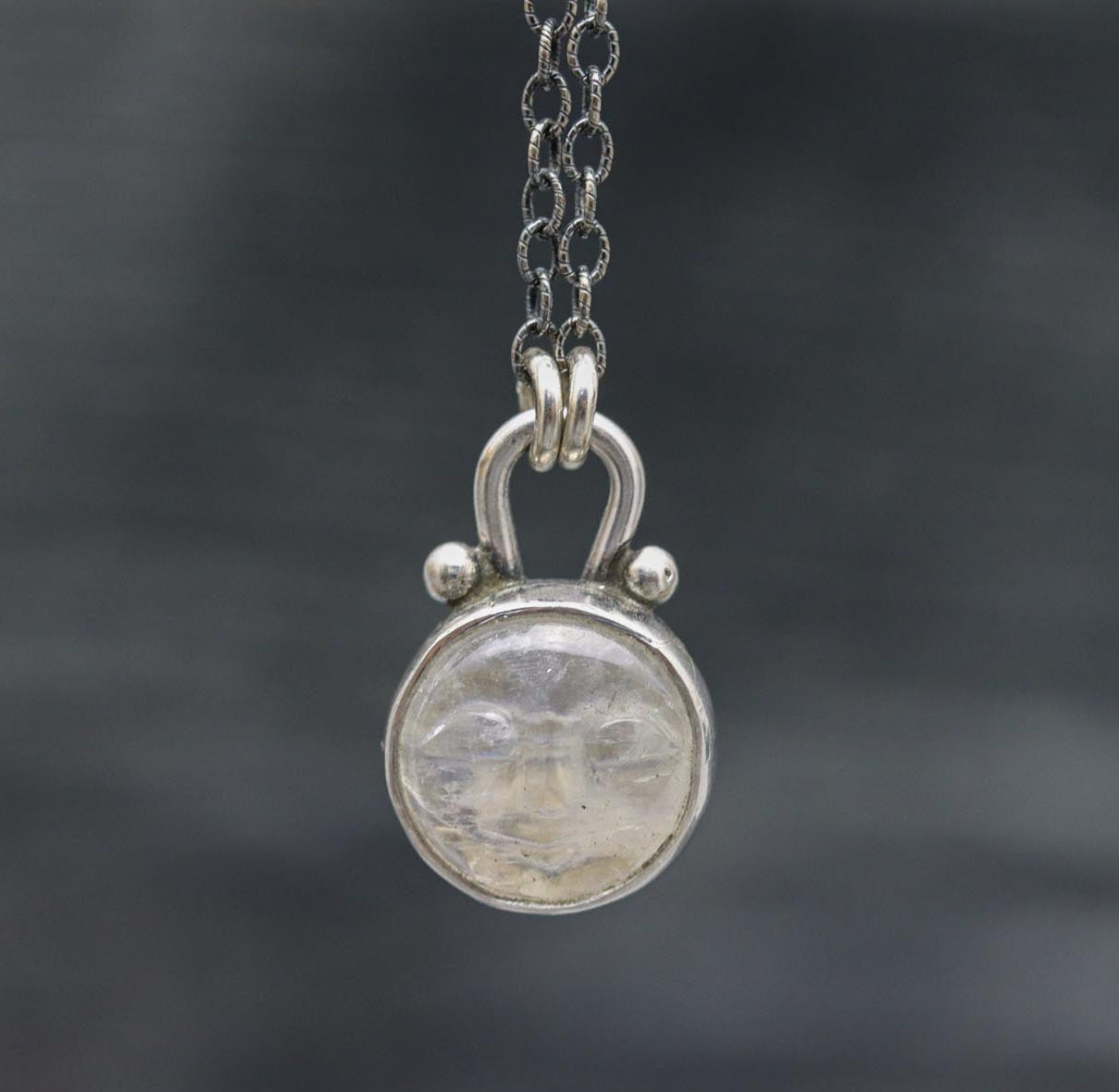 A sterling silver pendant necklace featuring a carved moonstone with a face, suspended from a textured cable link chain.