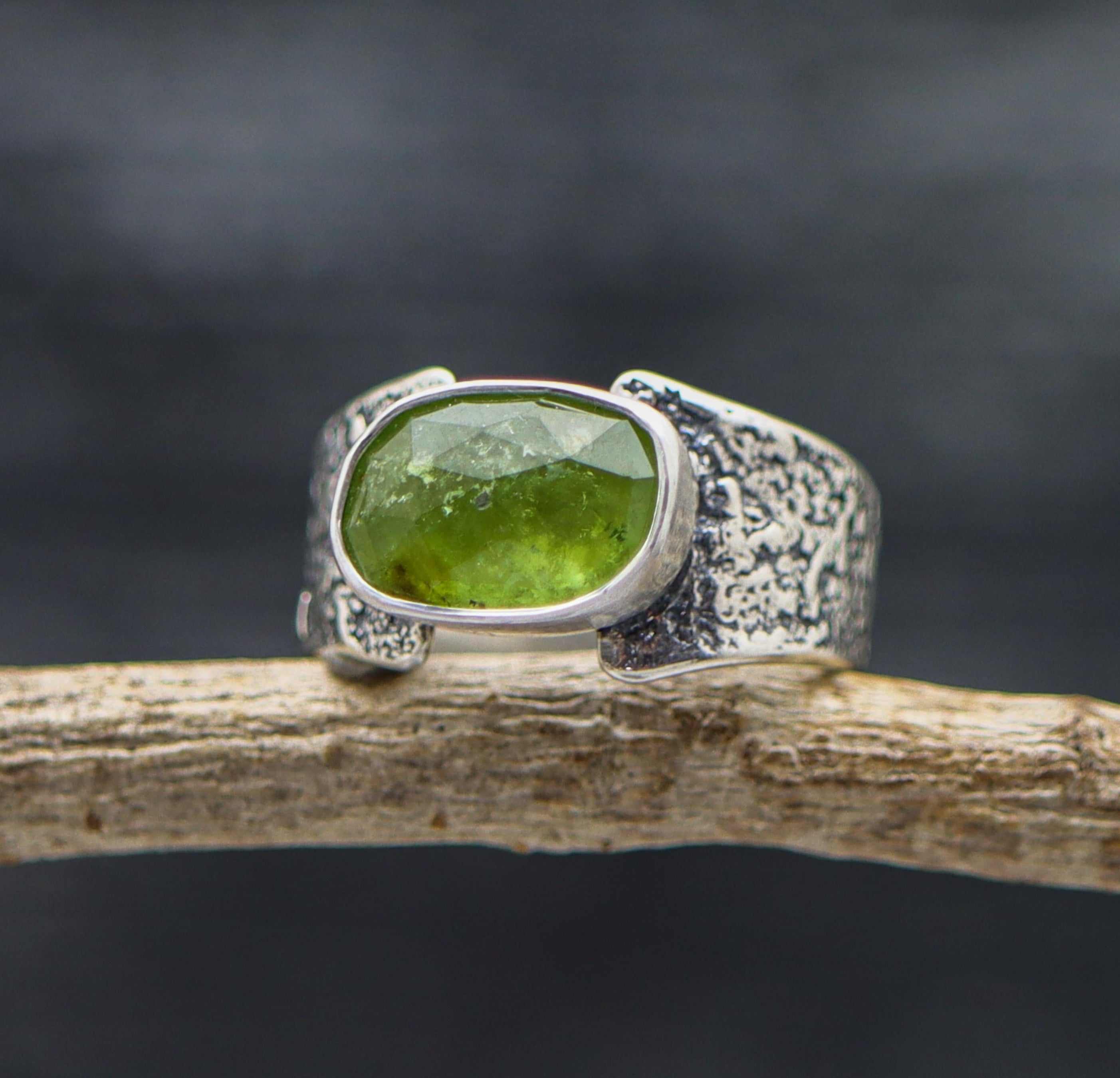 A wide band sterling silver ring with a faceted rose cut green tourmaline centerpiece.