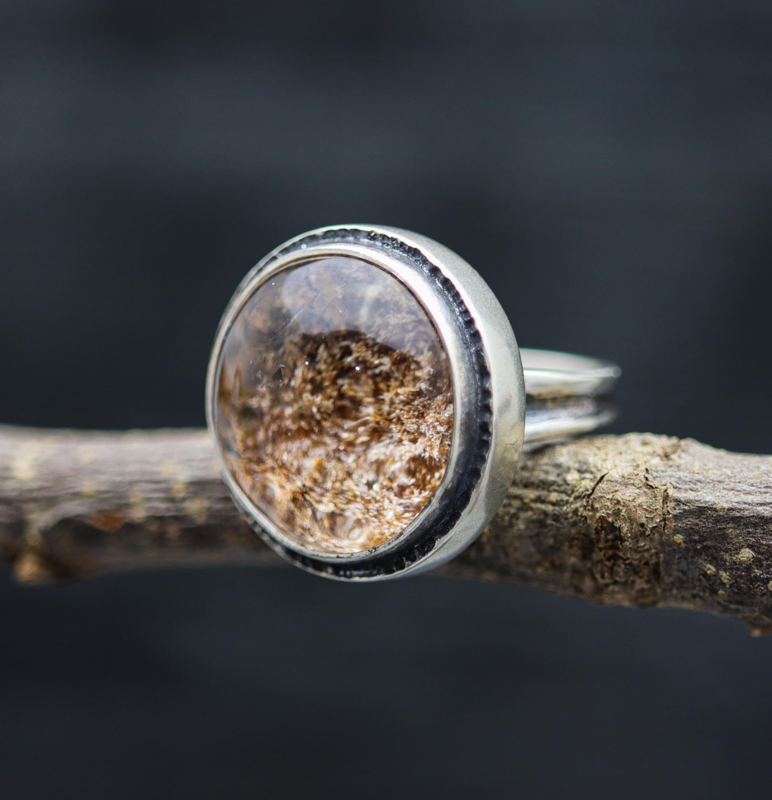 Silver ring with a natural stone on a branch against a dark background