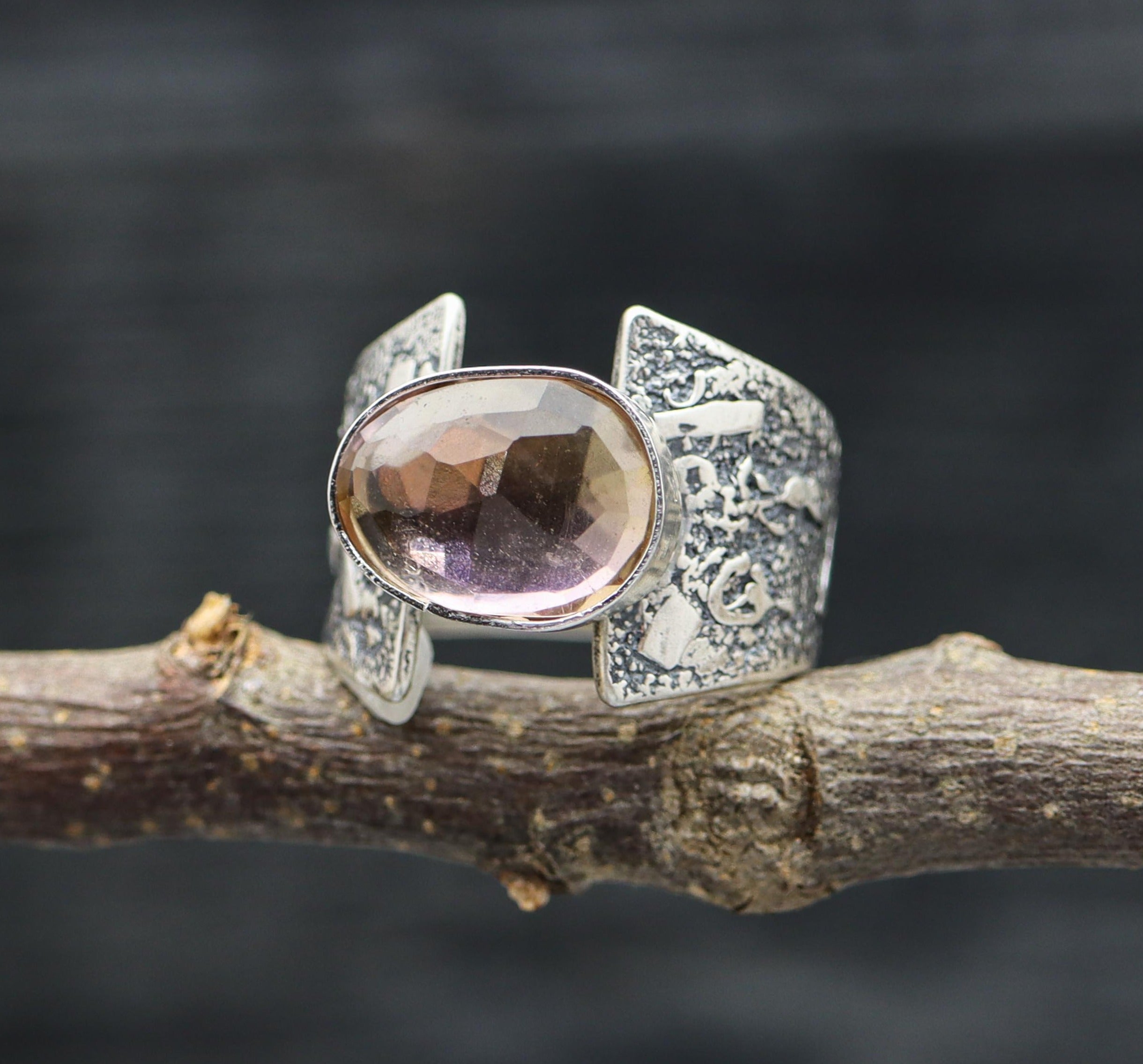 A sterling silver ring with a central ametrine gemstone, displayed on a rustic branch background.