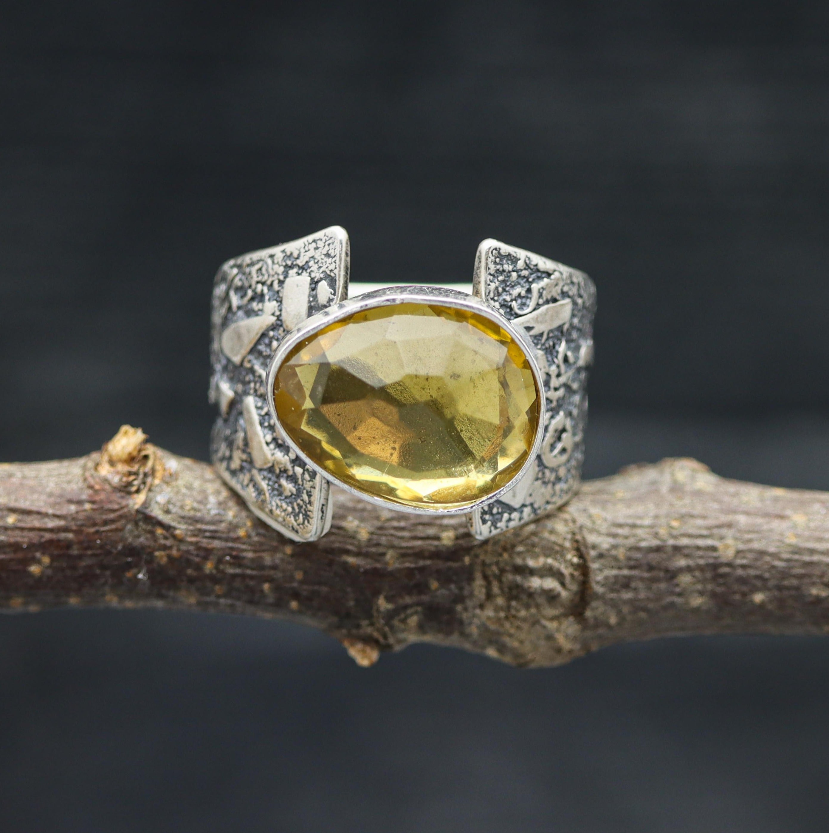 A sterling silver ring with a faceted yellow citrine gemstone, set on a branch against a dark background.