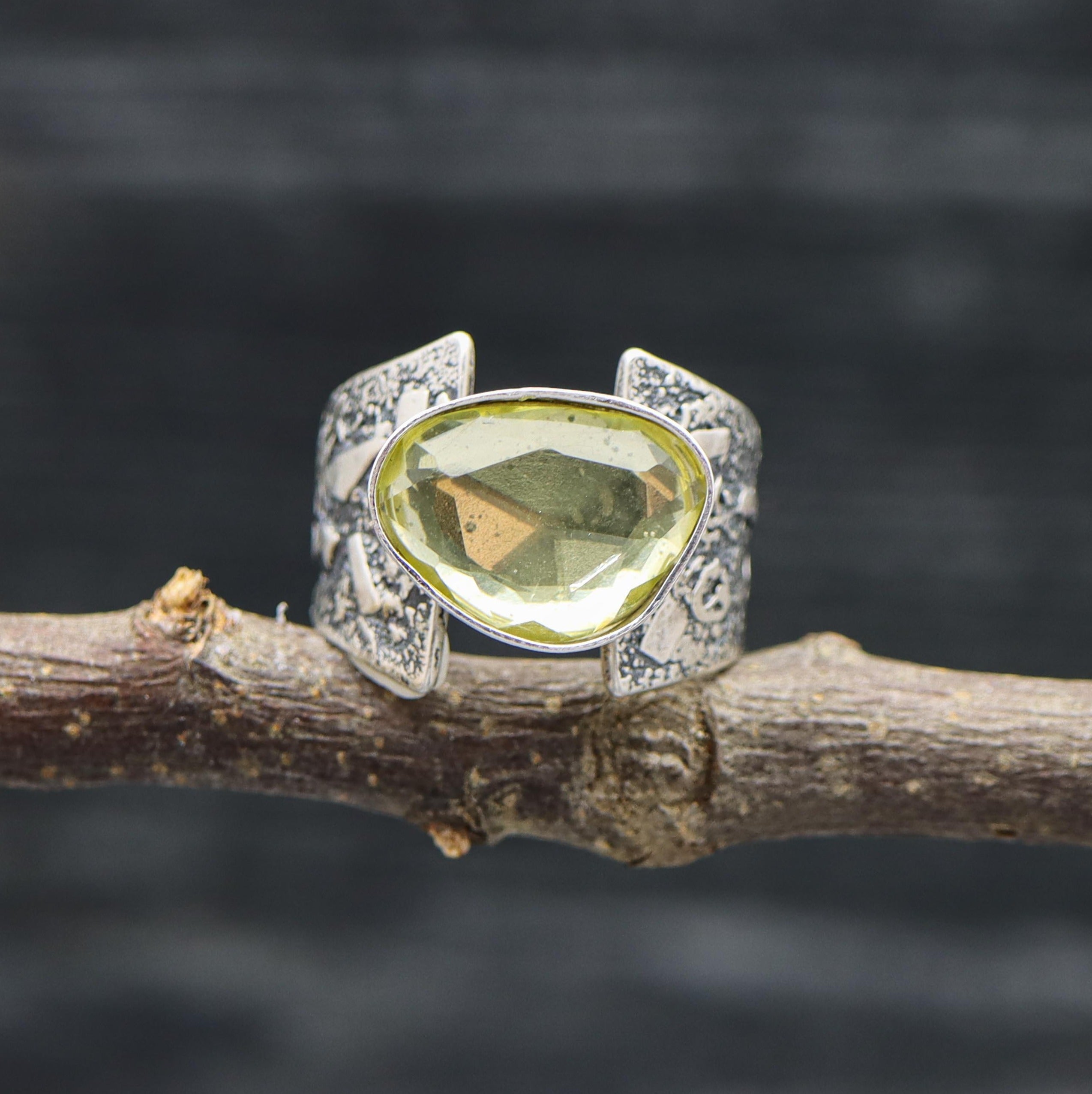 A sterling silver ring with a lemon quartz gemstone, set in a rose cut setting, displayed on a branch against a dark background.