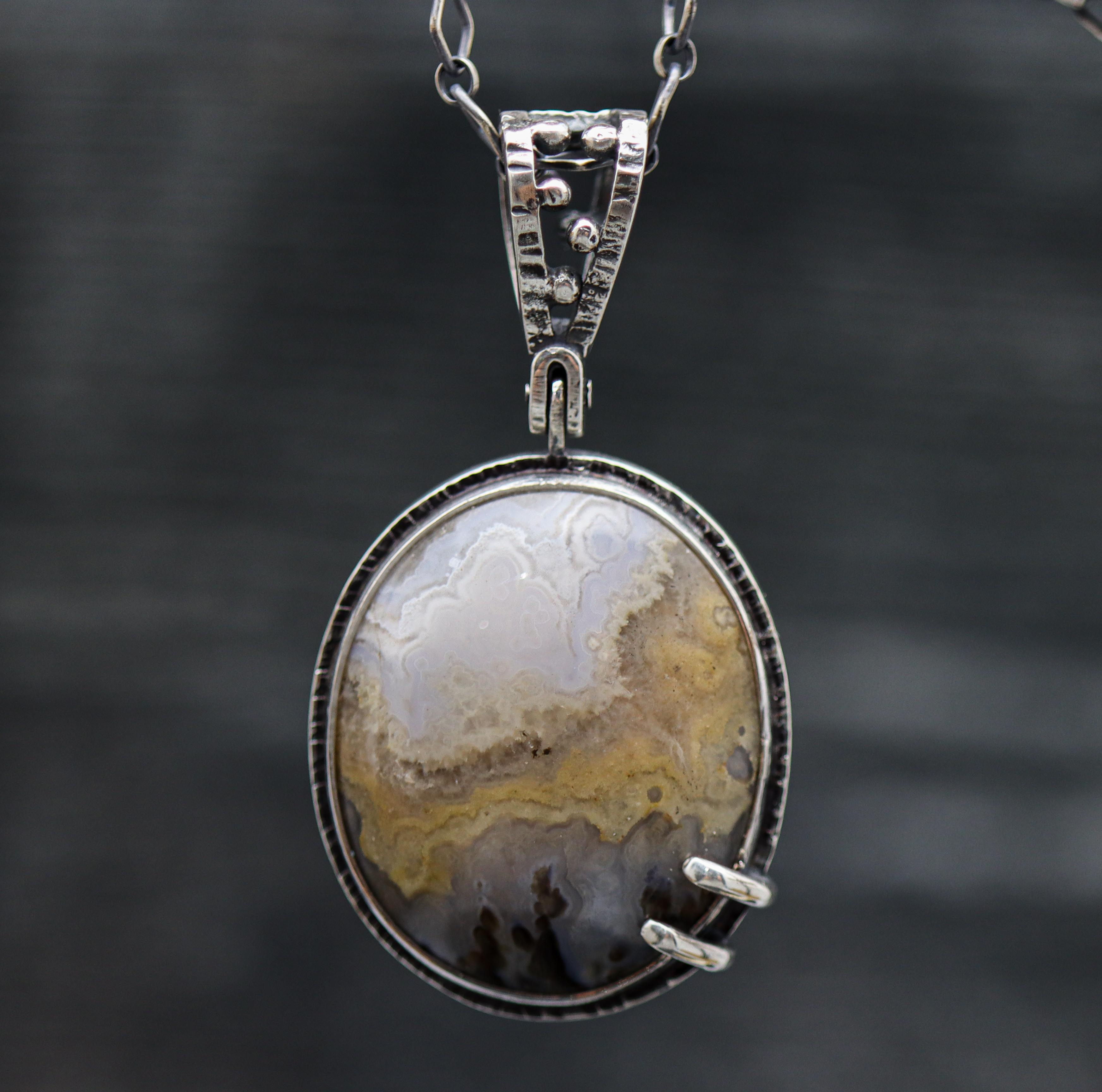 A sterling silver pendant featuring a Prudent Man Agate gemstone, suspended by a silver chain against a dark background.