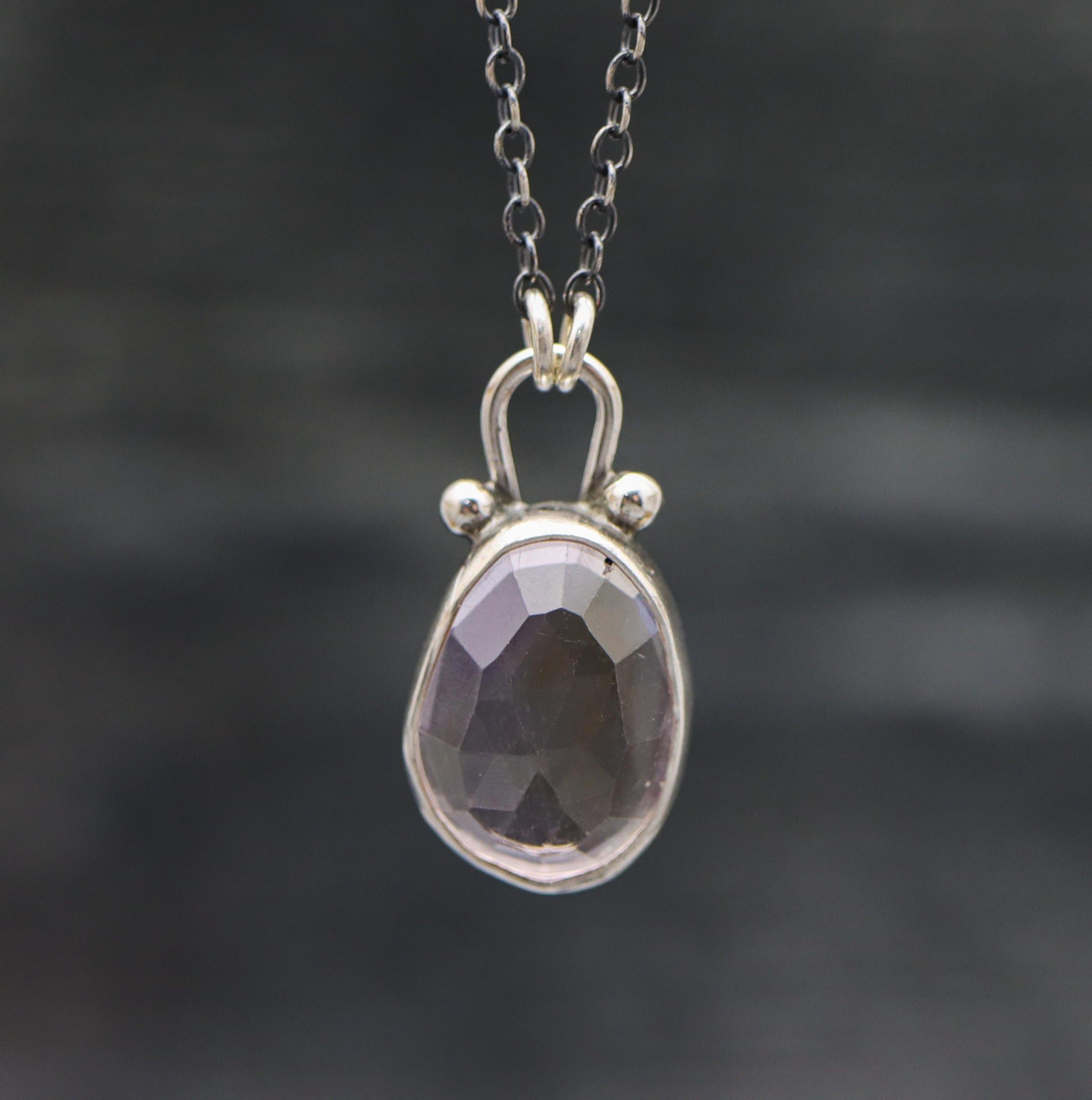 A sterling silver pendant necklace featuring a faceted rose cut ametrine, with small silver ball accents, suspended from a silver chain.